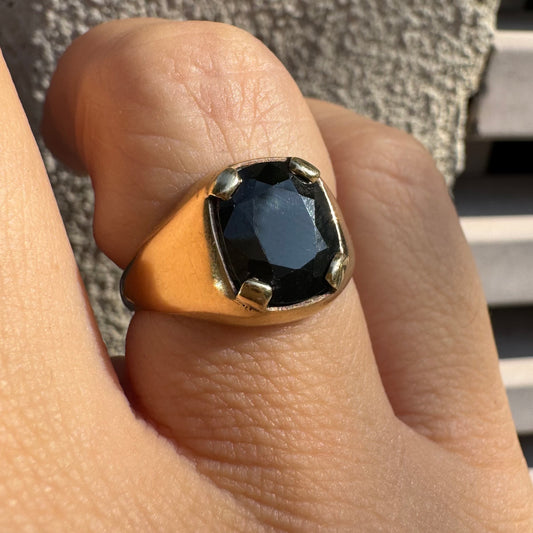 טבעת זהב 9 קראט משובצת ספיר ירוק כהה בחיתוך כרית ובתפסים עבים, בעיצוב נקי ובעל נוכחות. 