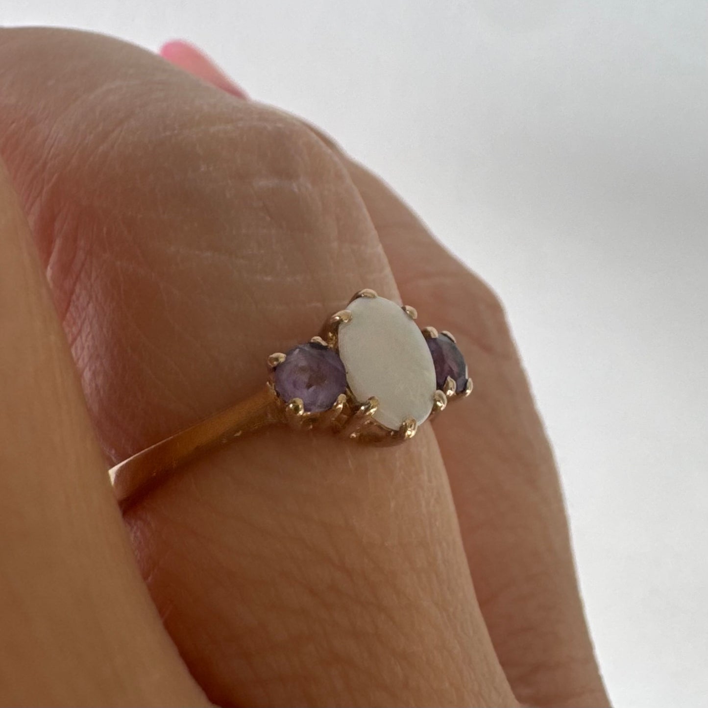 9K gold ring set with an oval Opal at the center, flanked by two delicate purple stones.