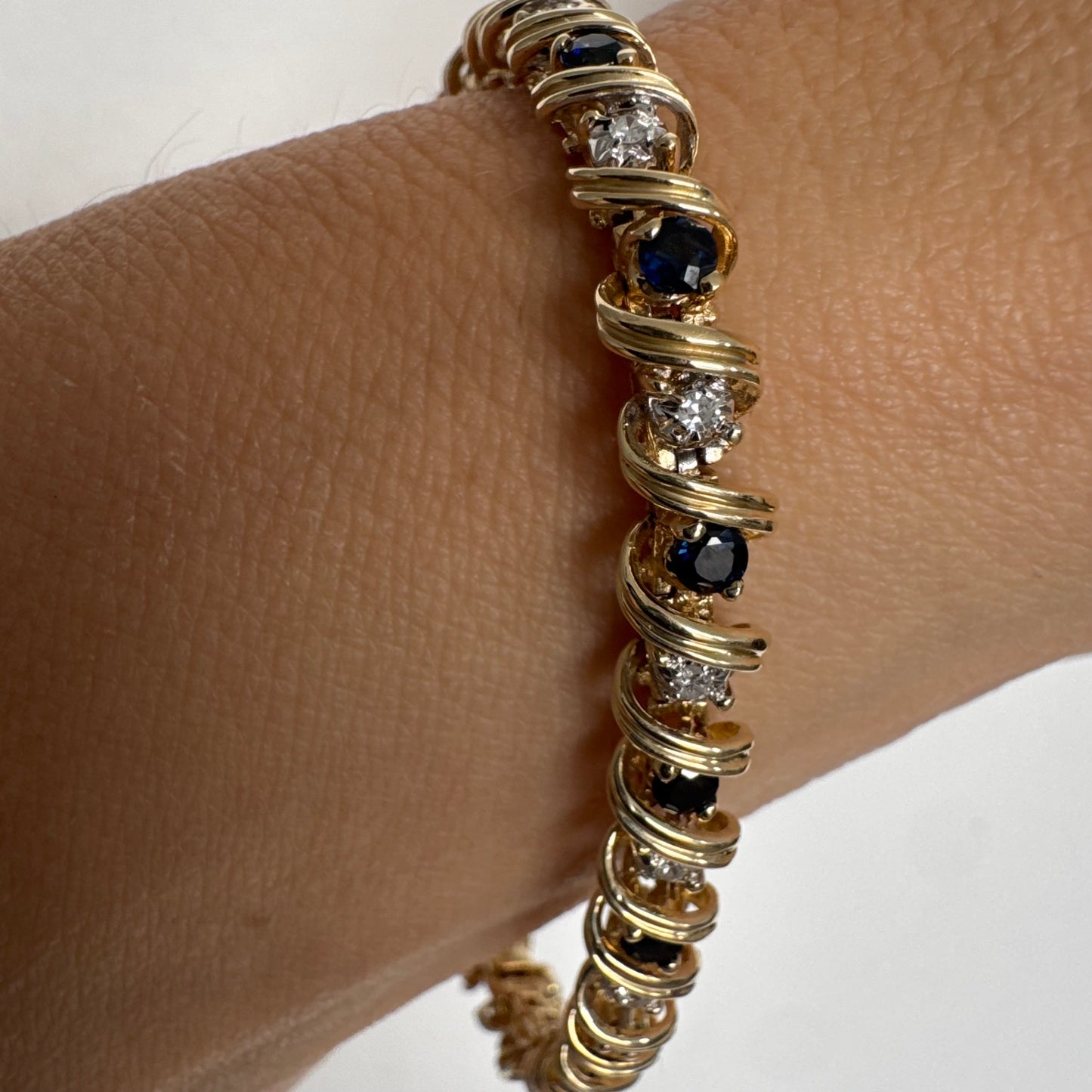 צמיד זהב צהוב 14 קראט משובץ אבני ספיר כחולות ויהלומים, המשובצים בעיצוב זורם עם קווים מעוגלים העוטפים כל אבן.