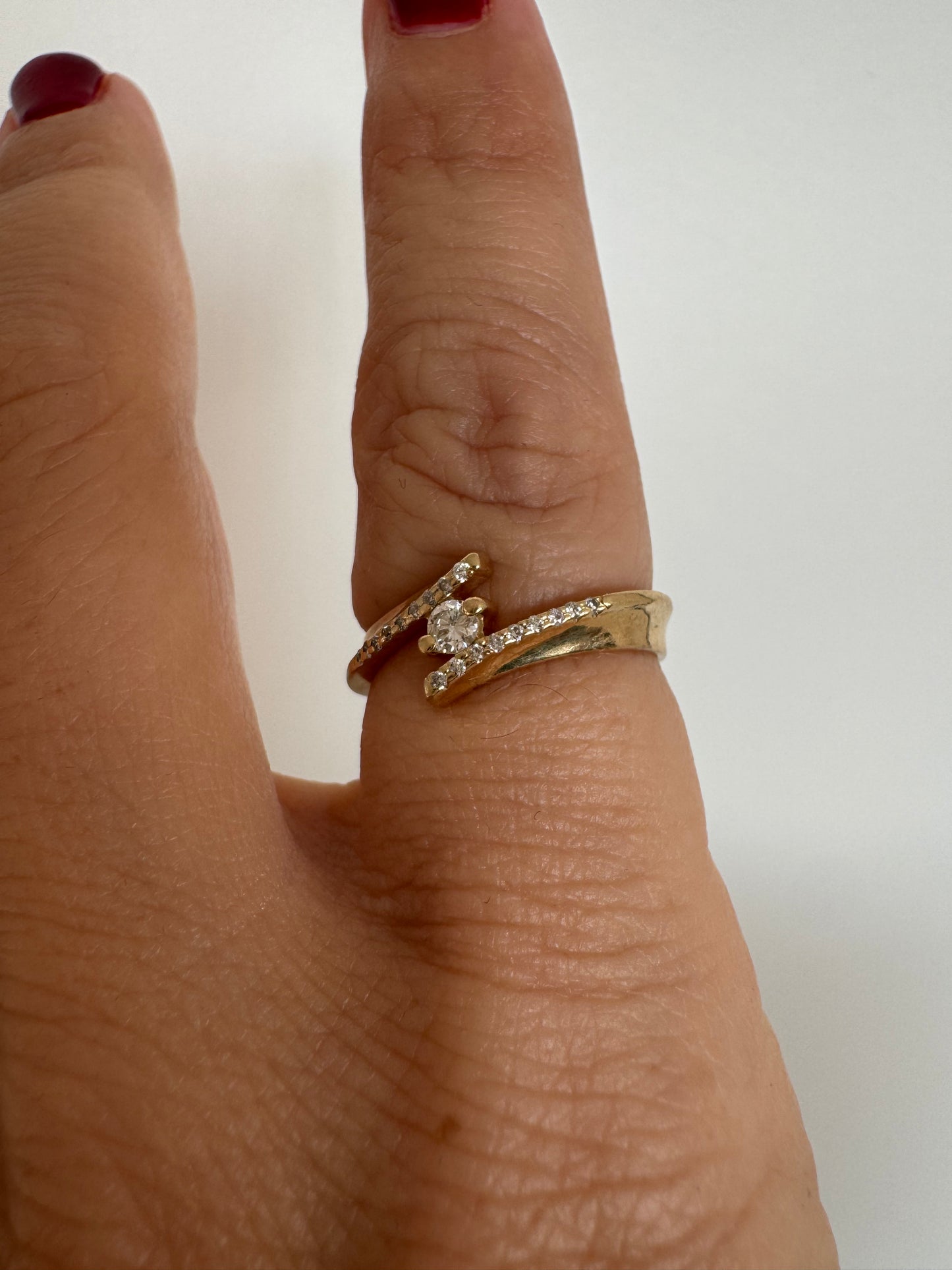 טבעת זהב 14 קראט בעיצוב פתוח ואלגנטי, משובצת יהלום מרכזי ויהלומים עדינים לאורך הזרועות.