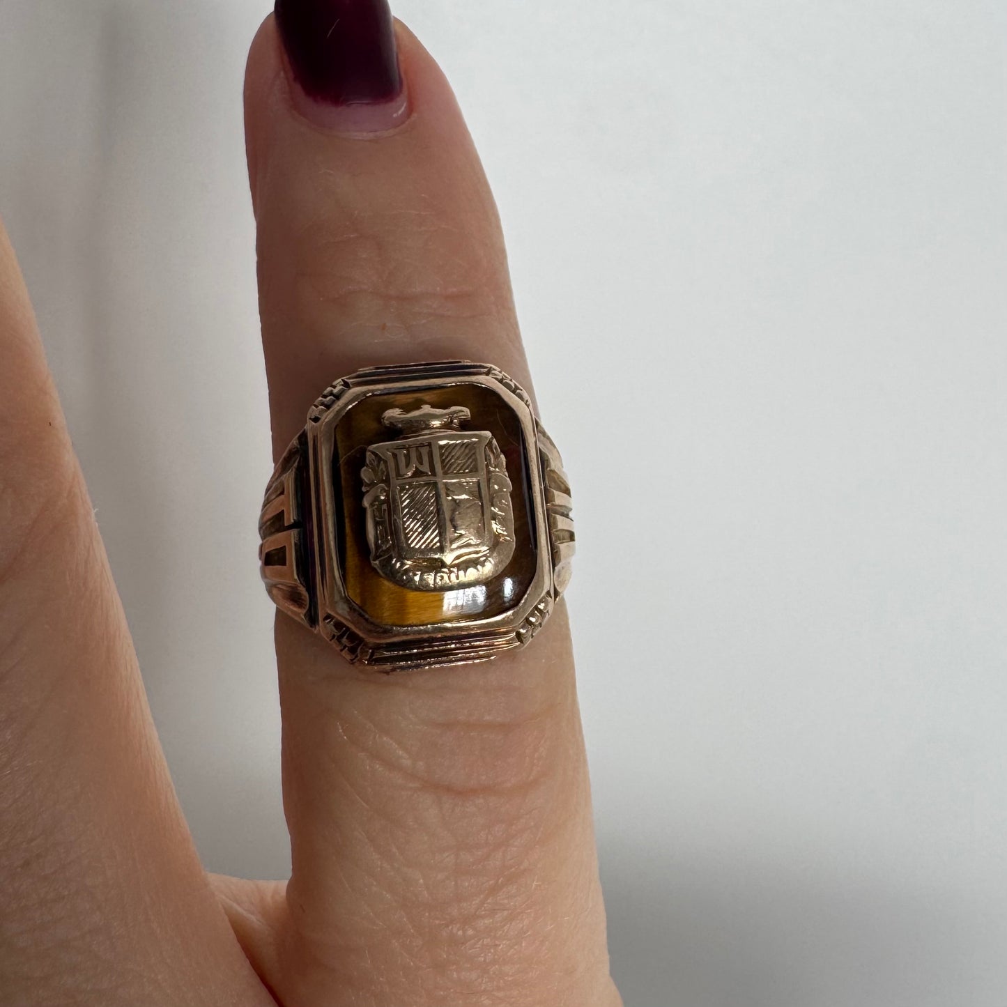 טבעת חותם זהב צהוב 10 קראט עם אבן בגוון חום-דבש ועיטור סמל מובלט במרכז.