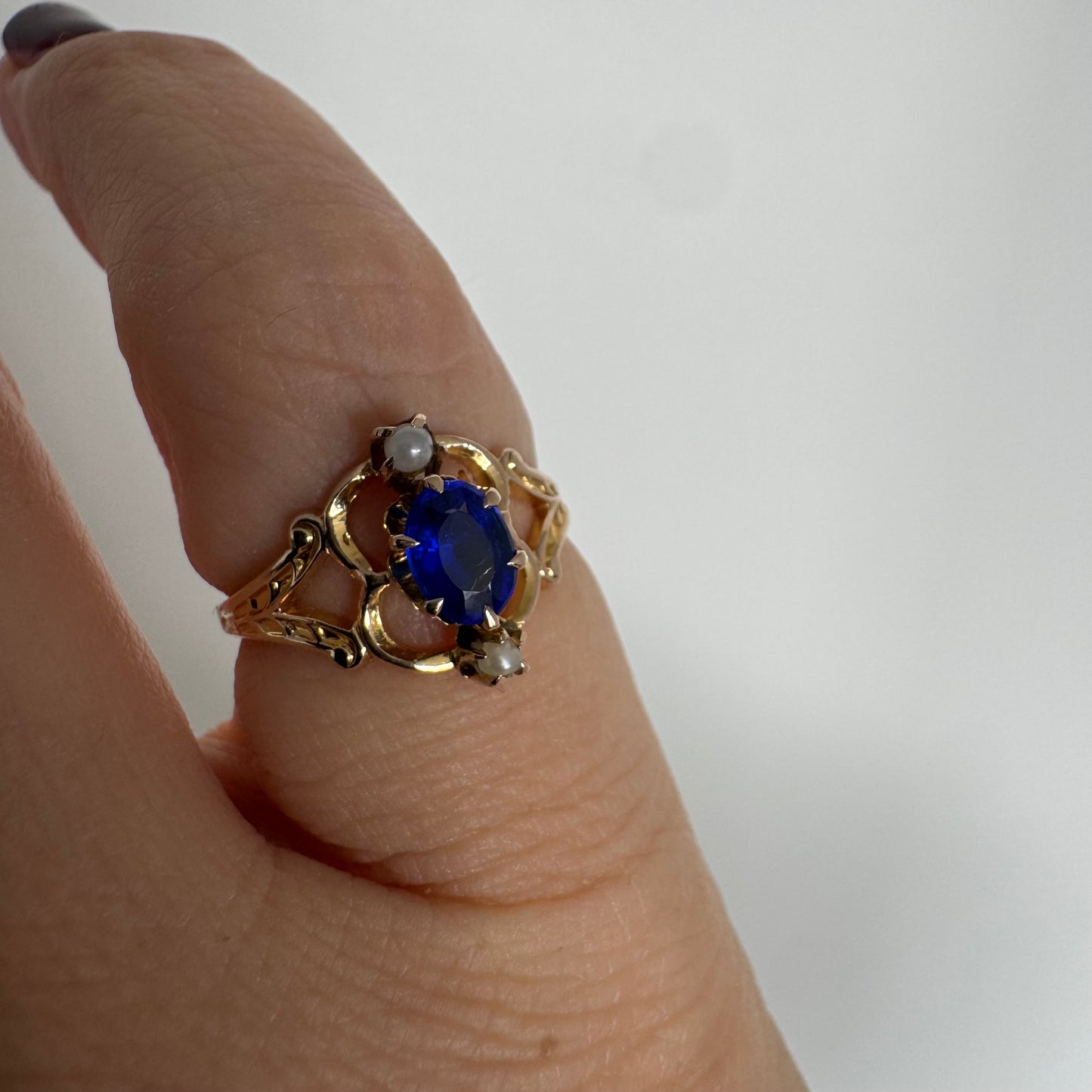 טבעת זהב צהוב 10 קראט משובצת אבן ספיר אובלית בגוון כחול עמוק ועשיר, ולצידה פנינים קטנות עדינות מעל ומתחת לאבן.