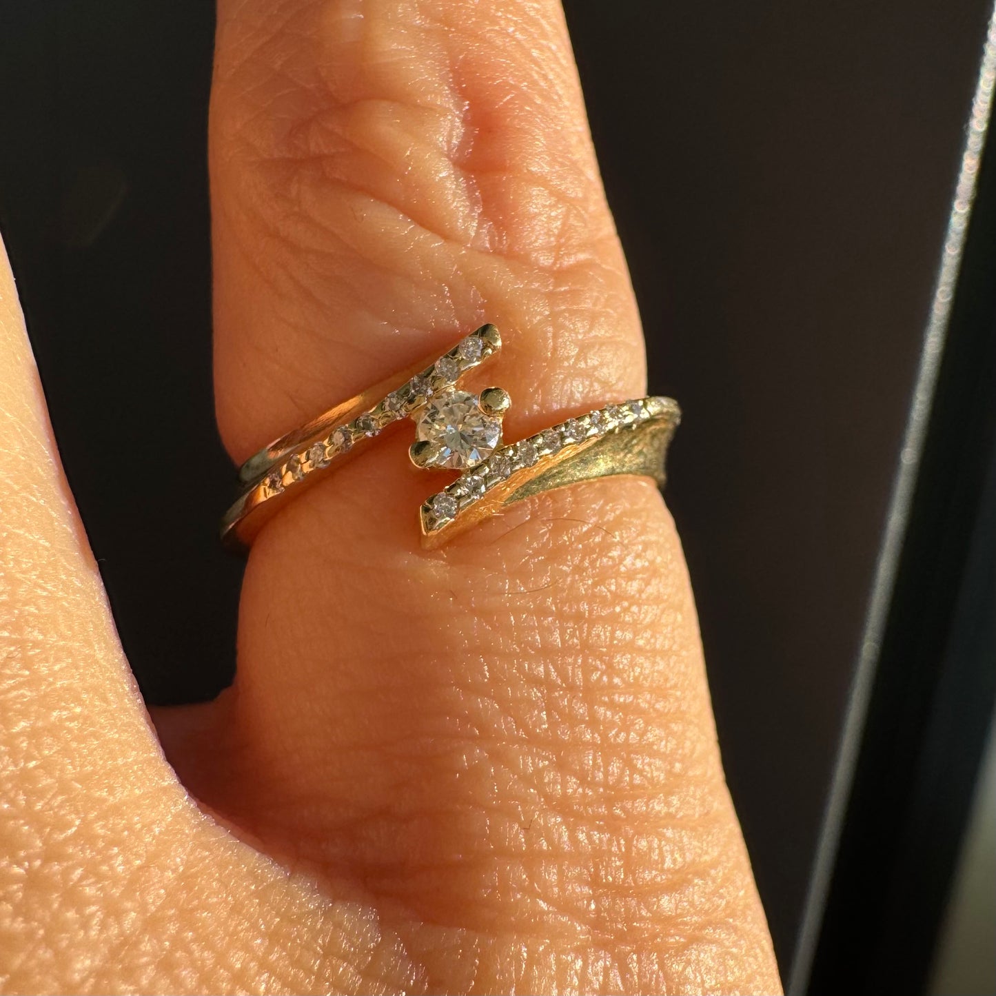 טבעת זהב 14 קראט בעיצוב פתוח ואלגנטי, משובצת יהלום מרכזי ויהלומים עדינים לאורך הזרועות.