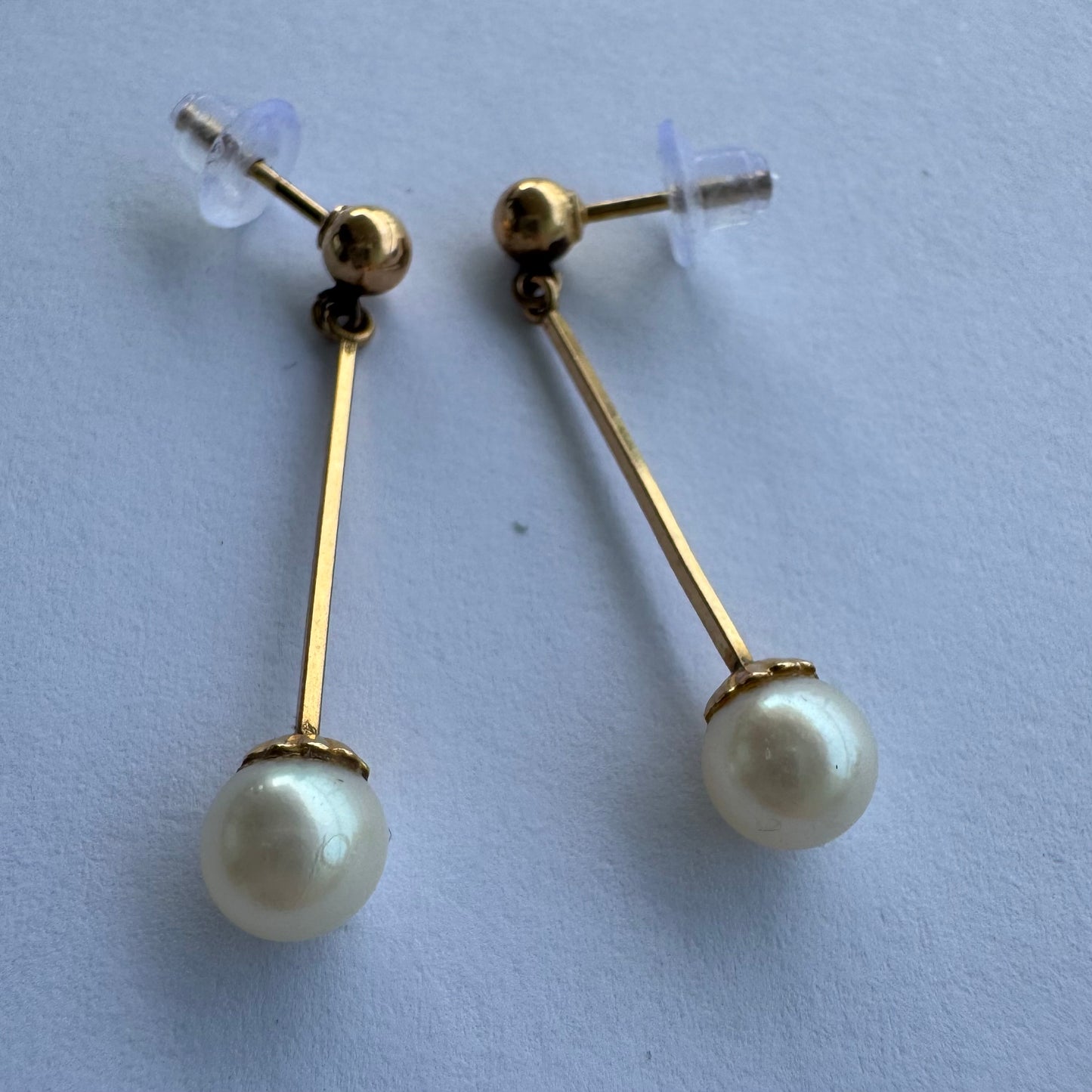 עגילי זהב 14 קראט בעיצוב תלוי ועדין, עם פנינה עגולה בקצה.