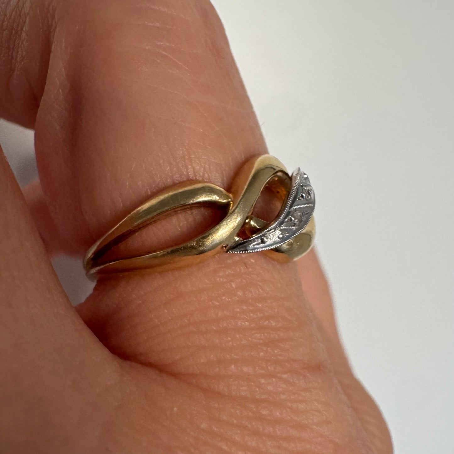 טבעת זהב צהוב 18 קראט בעיצוב קשר קלאסי, בשילוב אלמנט מרכזי מזהב לבן משובץ יהלומים עדינים.