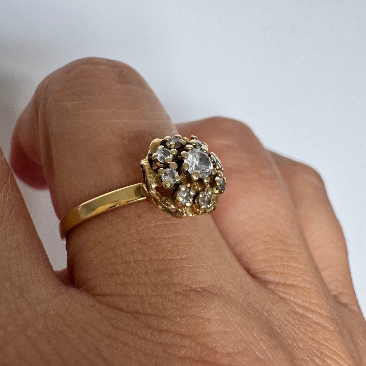 18K gold ring set with sparkling clear gemstones in a delicate floral cluster design.