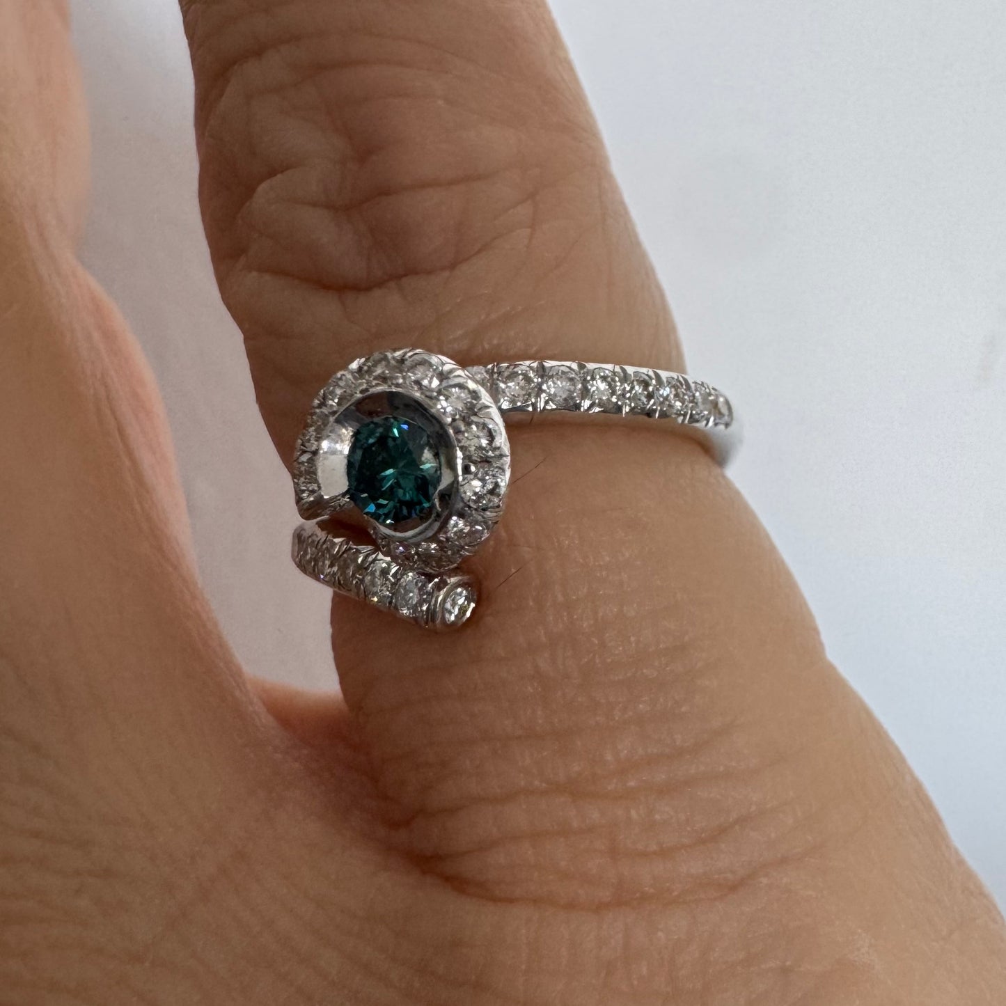 טבעת זהב לבן 18 במרכזה משובץ יהלום כחול עז, מוקף בהילה של יהלומים לבנים והזרועות של הטבעת משובצות יהלומים