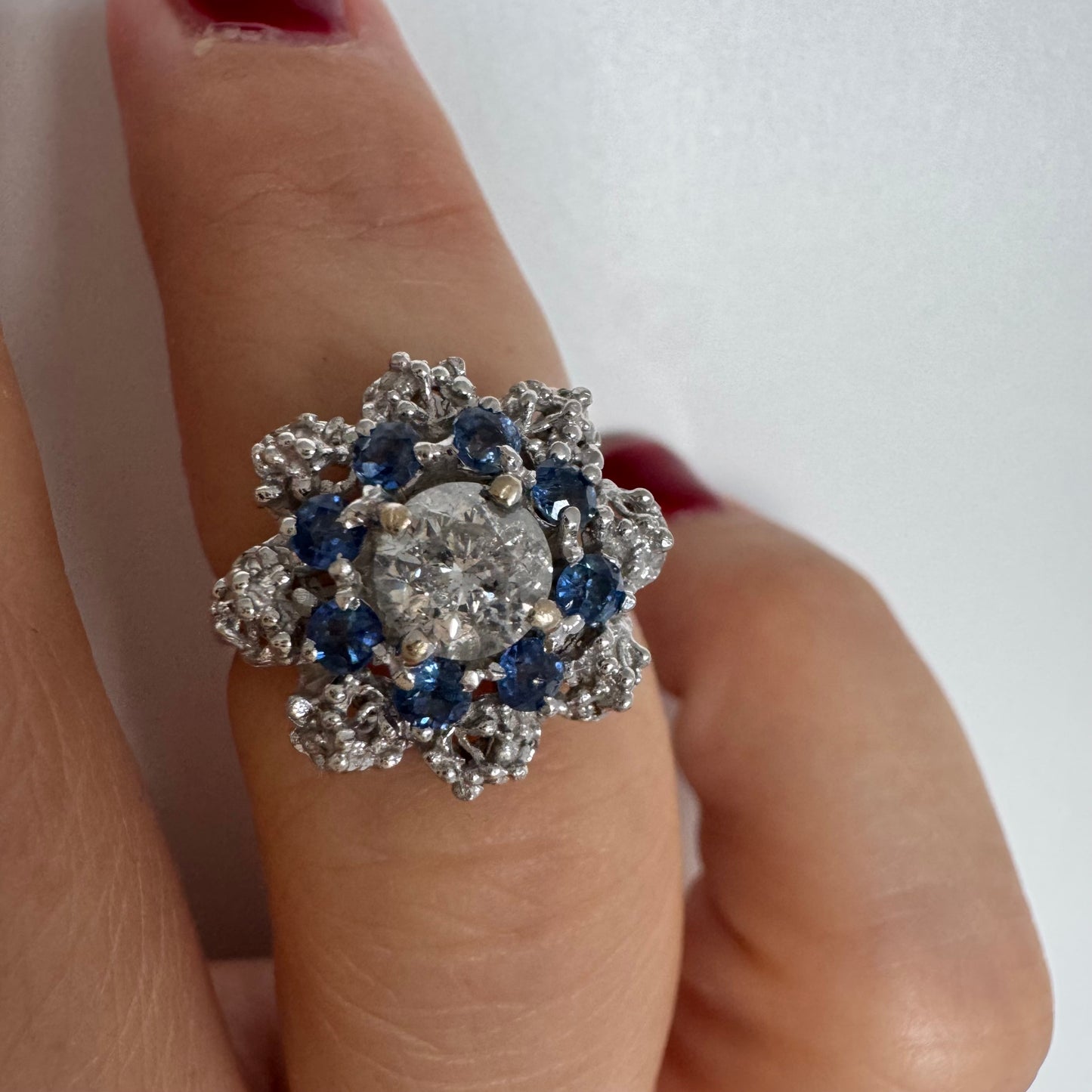 18K gold ring featuring a large round Diamond at the center, surrounded by a floral halo of purple -blue Tanzanite and & Diamonds.