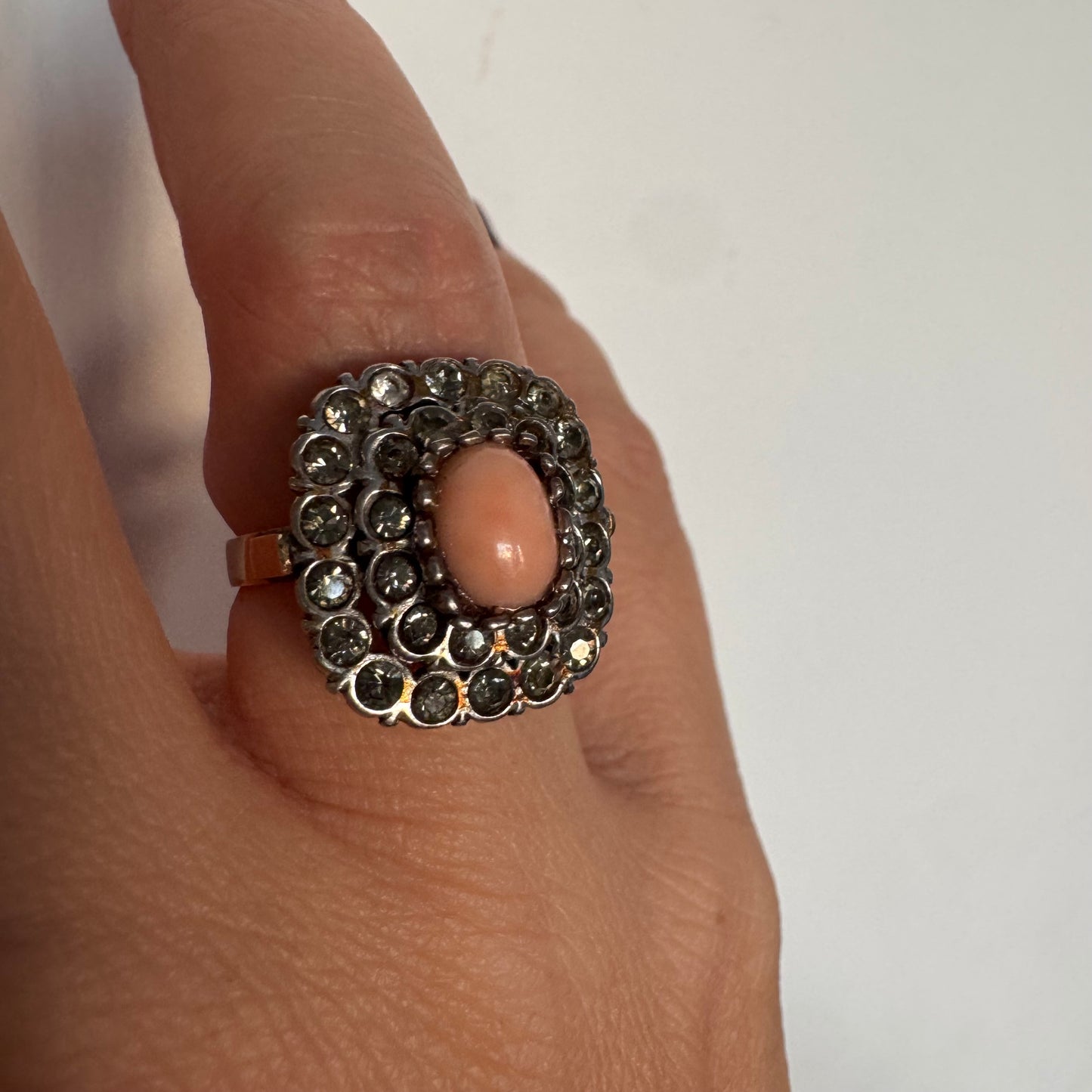 טבעת וינטג׳ עם חלק תחתון מזהב 14 קראט וחלק עליון עשוי כסף משובצת אבן קורל טבעית במרכז ומסביבה אבנים בהירות שאינן יהלומים.