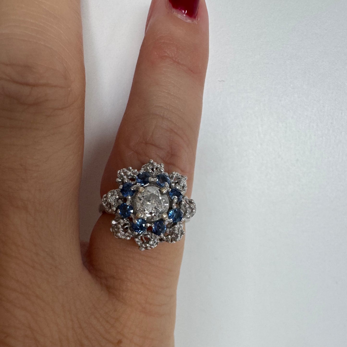 18K gold ring featuring a large round Diamond at the center, surrounded by a floral halo of purple -blue Tanzanite and & Diamonds.
