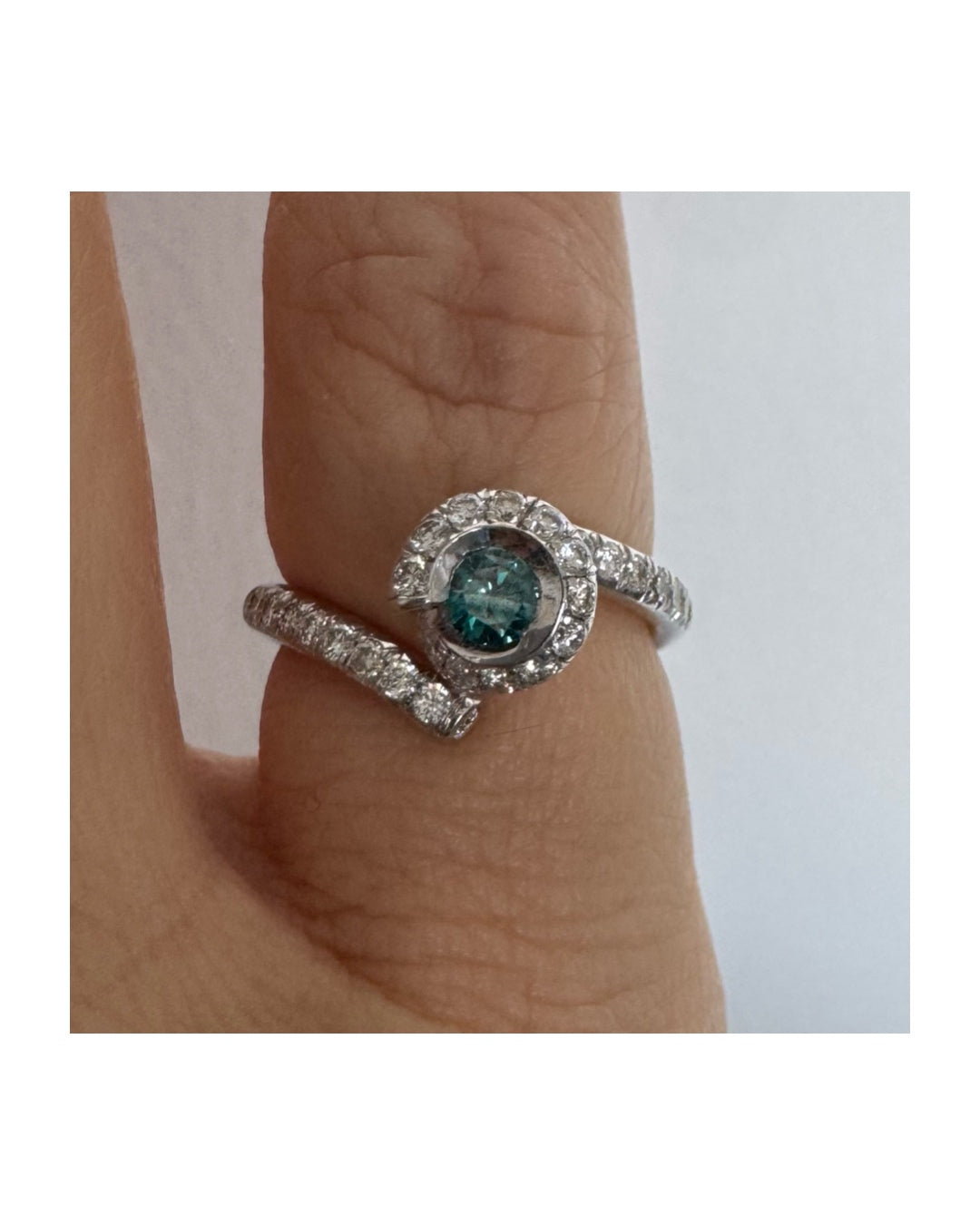 טבעת זהב לבן 18 במרכזה משובץ יהלום כחול עז, מוקף בהילה של יהלומים לבנים והזרועות של הטבעת משובצות יהלומים