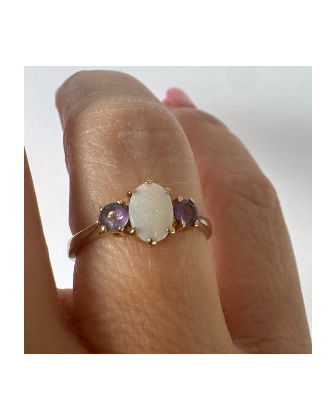 9K gold ring set with an oval Opal at the center, flanked by two delicate purple stones.
