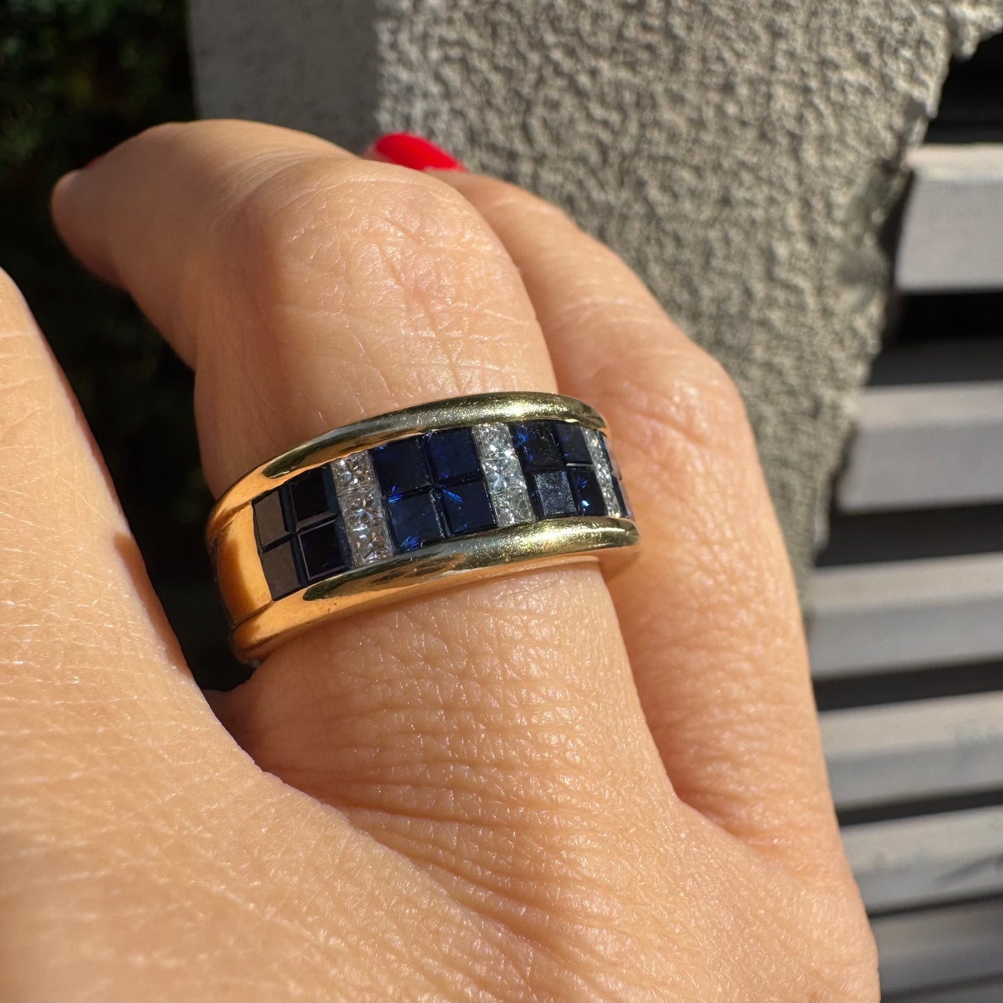 טבעת ה.שטרן זהב צהוב 18 קראט, בעיצוב רחב ומרשים. משובצת שורת אבני ספיר כחולות מרובעות בשילוב מחיצות של יהלומים לנגיעת ברק יוקרתי.