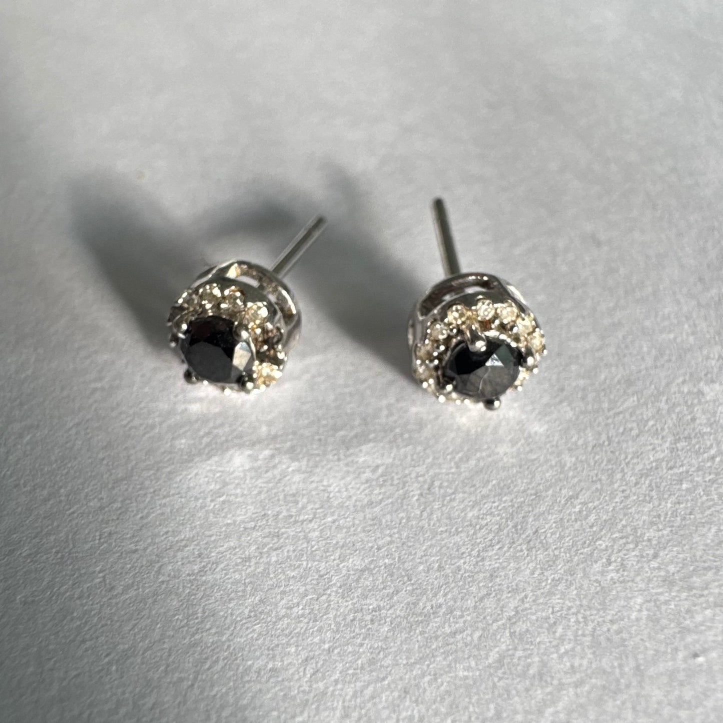 עגילי זהב לבן 10 קראט צמודים לאוזן, משובצים יהלומים שחורים עגולים במרכז ומסביבם הילה של יהלומים לבנים מנצנצים.