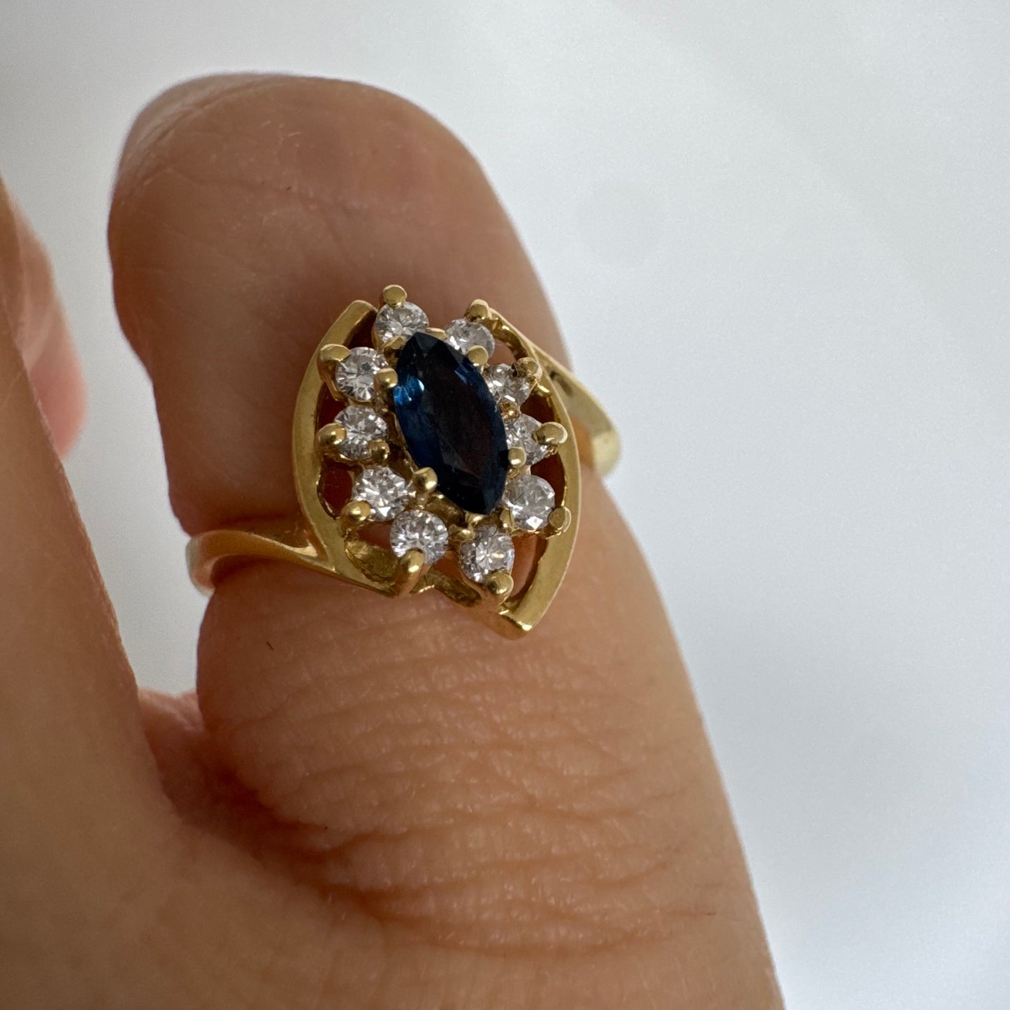 טבעת זהב צהוב 18 קראט משובצת ספיר כחול מרכזי בחיתוך מרקיזה, מוקף הילה של יהלומים המעניקים ניצוץ עדין ומדגישים את צבע האבן העמוק.