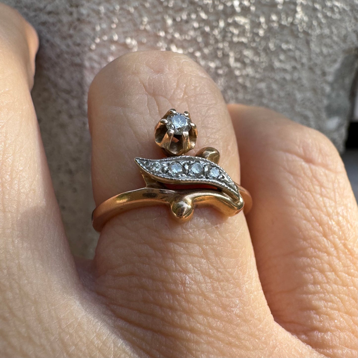 טבעת זהב אדום 14 קראט, עם שיבוץ בצורת פרח קטן ובו יהלום נוצץ לצד אלמנט מעוגל בצורת עלה משובץ יהלומים.