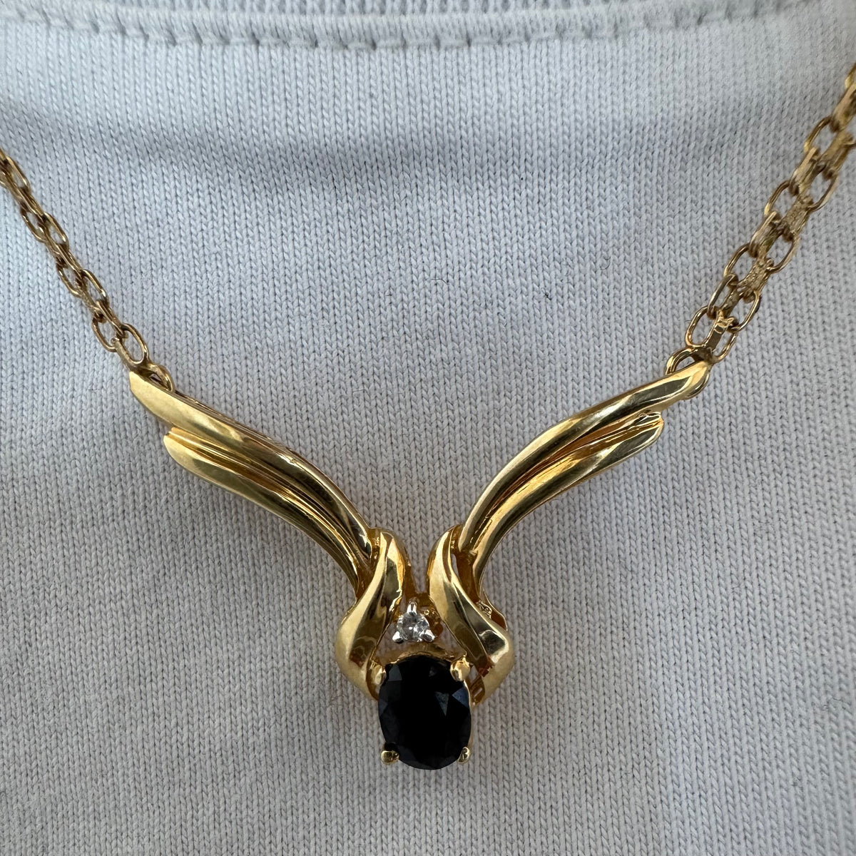 14K gold necklace featuring a flowing pendant design, set with a dark blue center Sapphire and a small Diamond above.