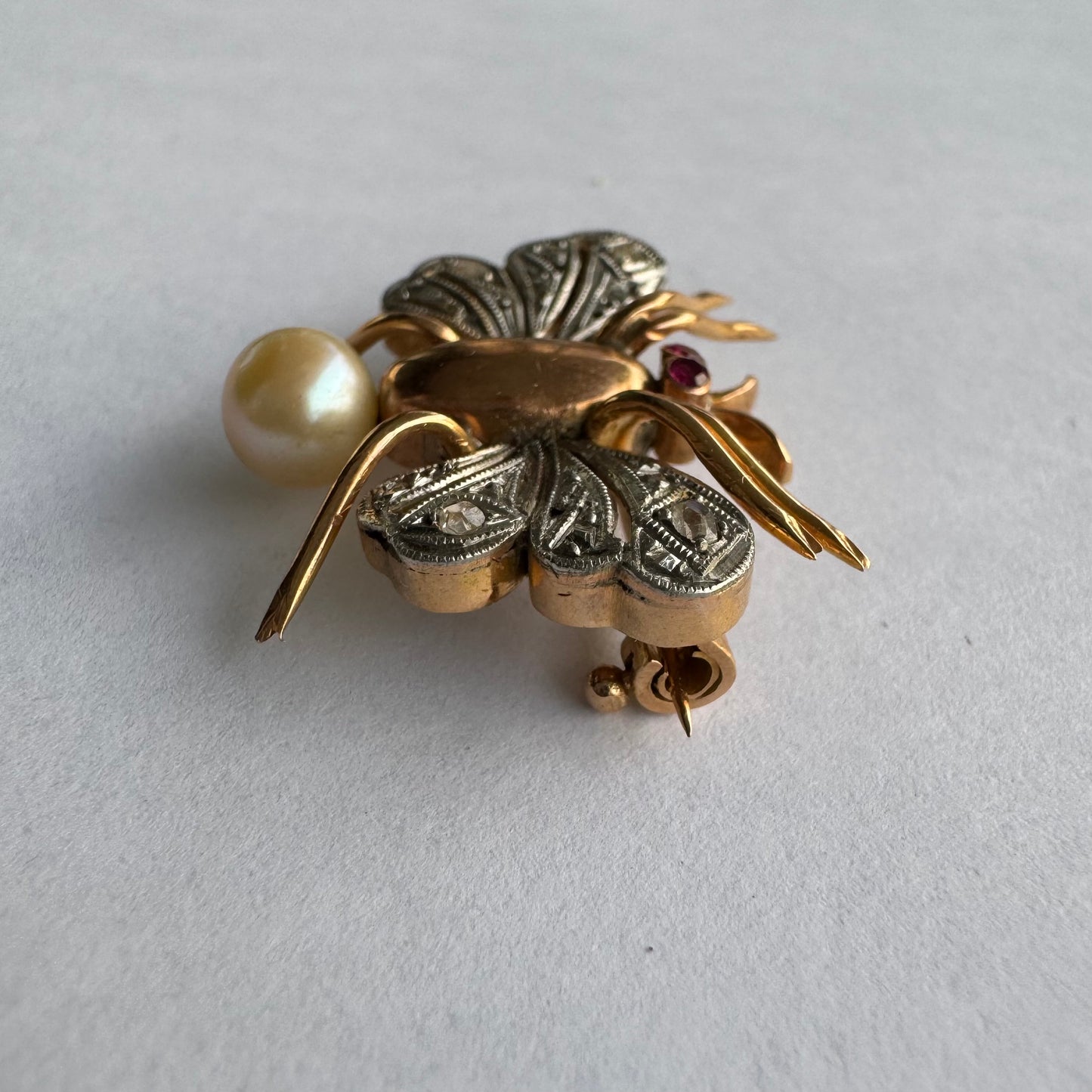 סיכת חרק ייחודית עשויה זהב 14 קראט משובצת יהלומים בעבודת פיליגרן עדינה בכנפיים, אבני רובי אדומות בעיניים ופנינה טבעית בגוון שמפניה.