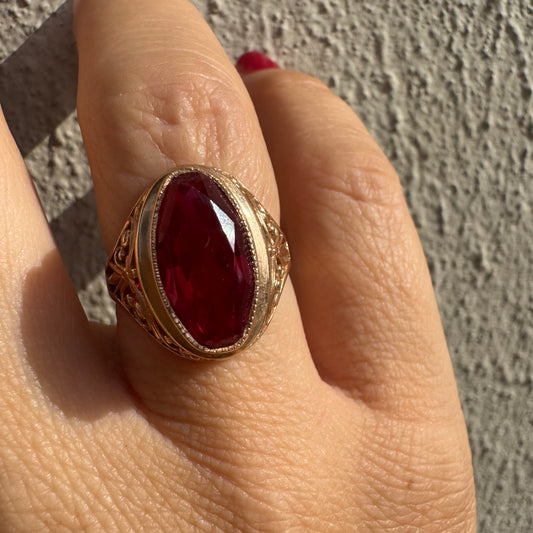 טבעת זהב צהוב 14 קראט משובצת אבן רובי אובלית בצבע אדום עמוק, במסגרת מעוטרת ובעבודת פיליגרן עדינה על הכתפיים.
