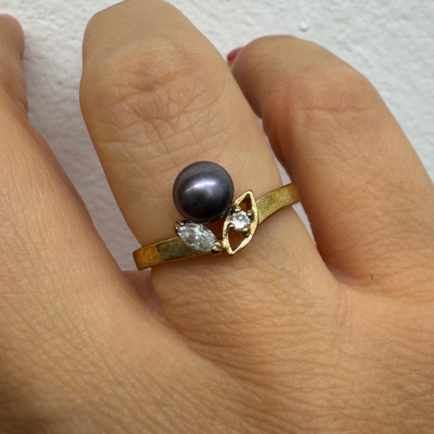 14K gold ring set with a Black Pearl at the center and clear gemstones on the sides.