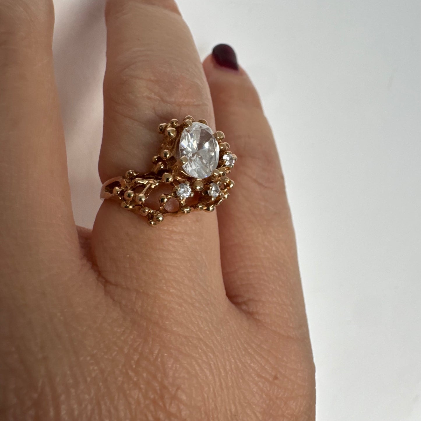14K gold ring set with a central oval clear stone, accented by additional clear stones in an open, organic design.