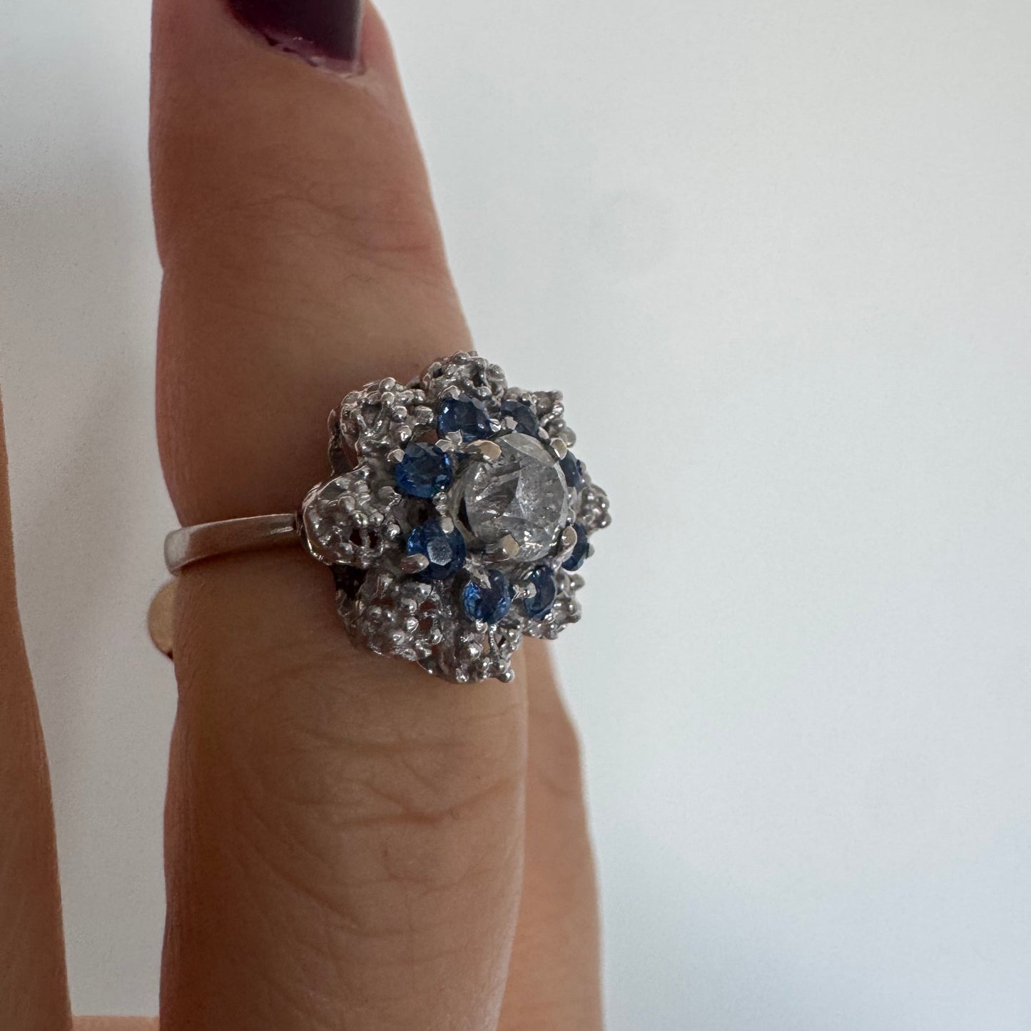 18K gold ring featuring a large round Diamond at the center, surrounded by a floral halo of purple -blue Tanzanite and & Diamonds.