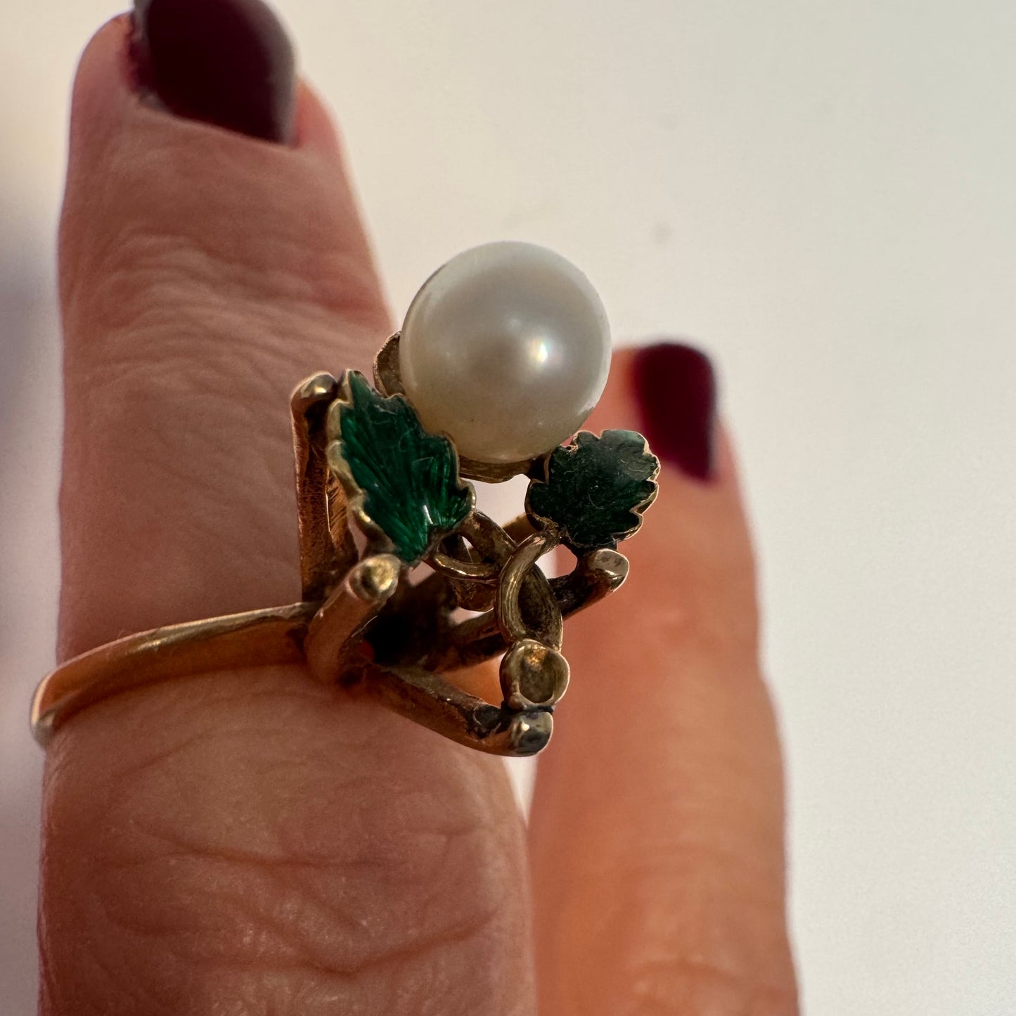 טבעת זהב 14 קראט משובצת פנינה מרכזית ומעוטרת אמייל ירוק בעבודת יד בצורת עלים.