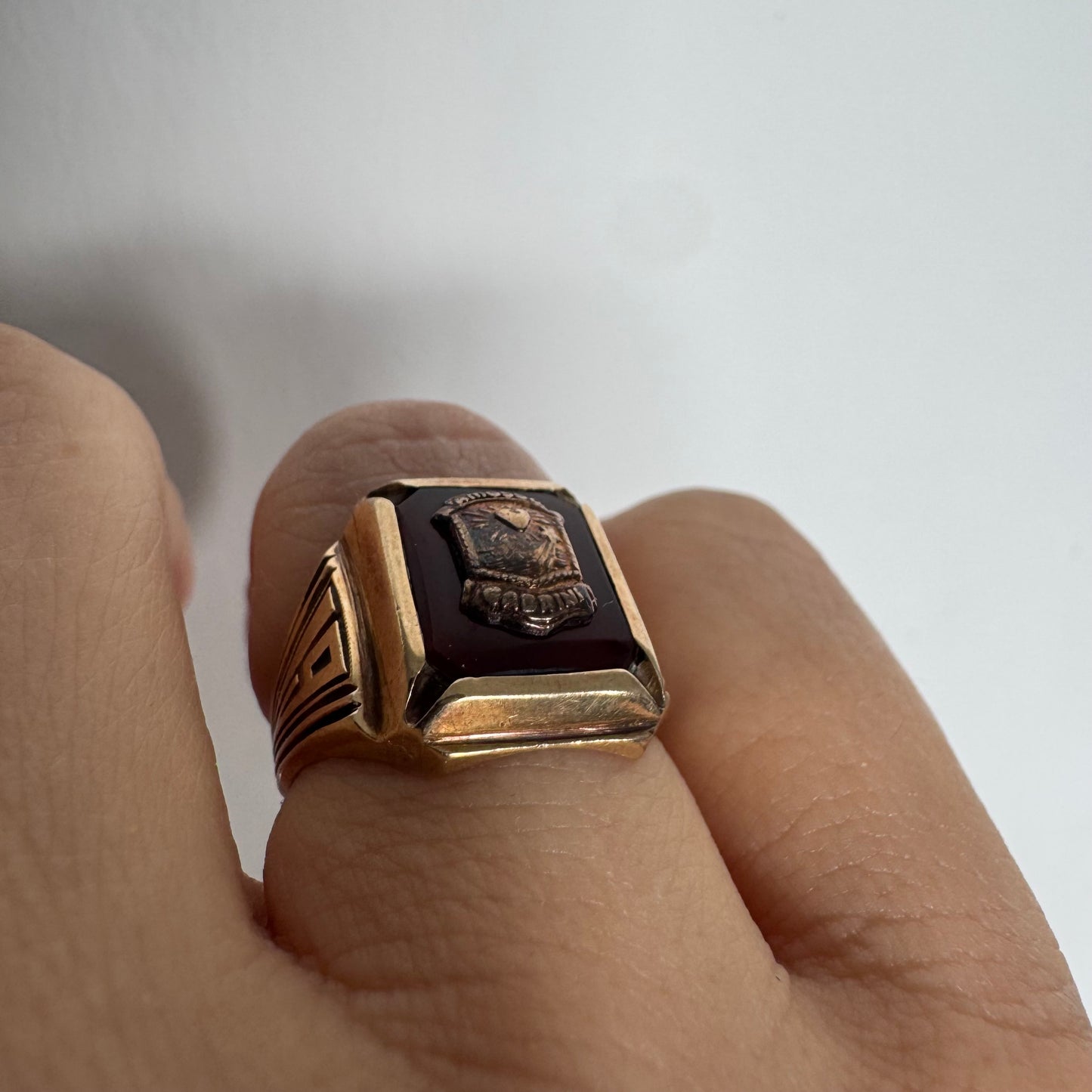 טבעת חותם זהב 10 קראט עם לוח מרכזי בגוון בורדו עמוק ועיטור סמל מובלט.