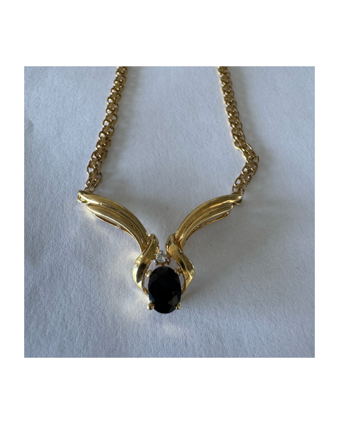 14K gold necklace featuring a flowing pendant design, set with a dark blue center Sapphire and a small Diamond above.