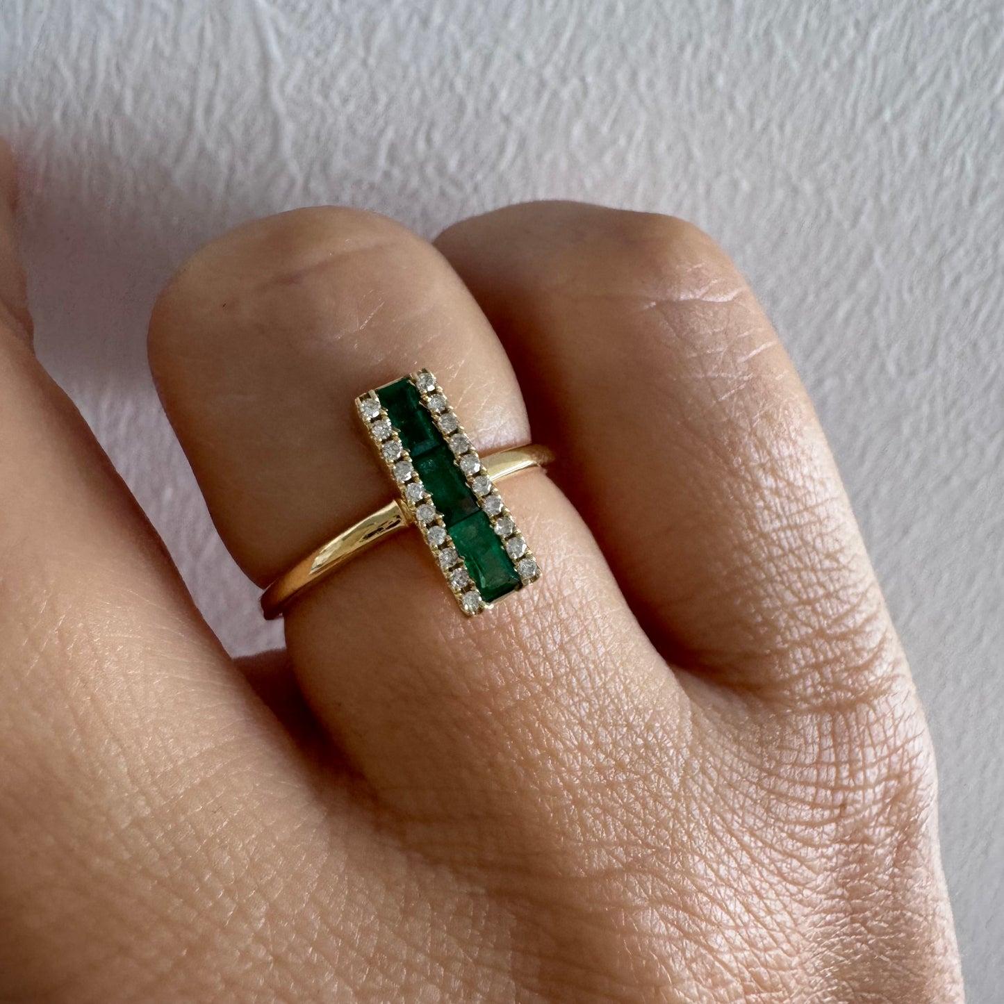 טבעת זהב 14 קראט משובצת אבני אמרלד בחיתוך באגט, מוקפות בשתי שורות של יהלומים נוצצים .