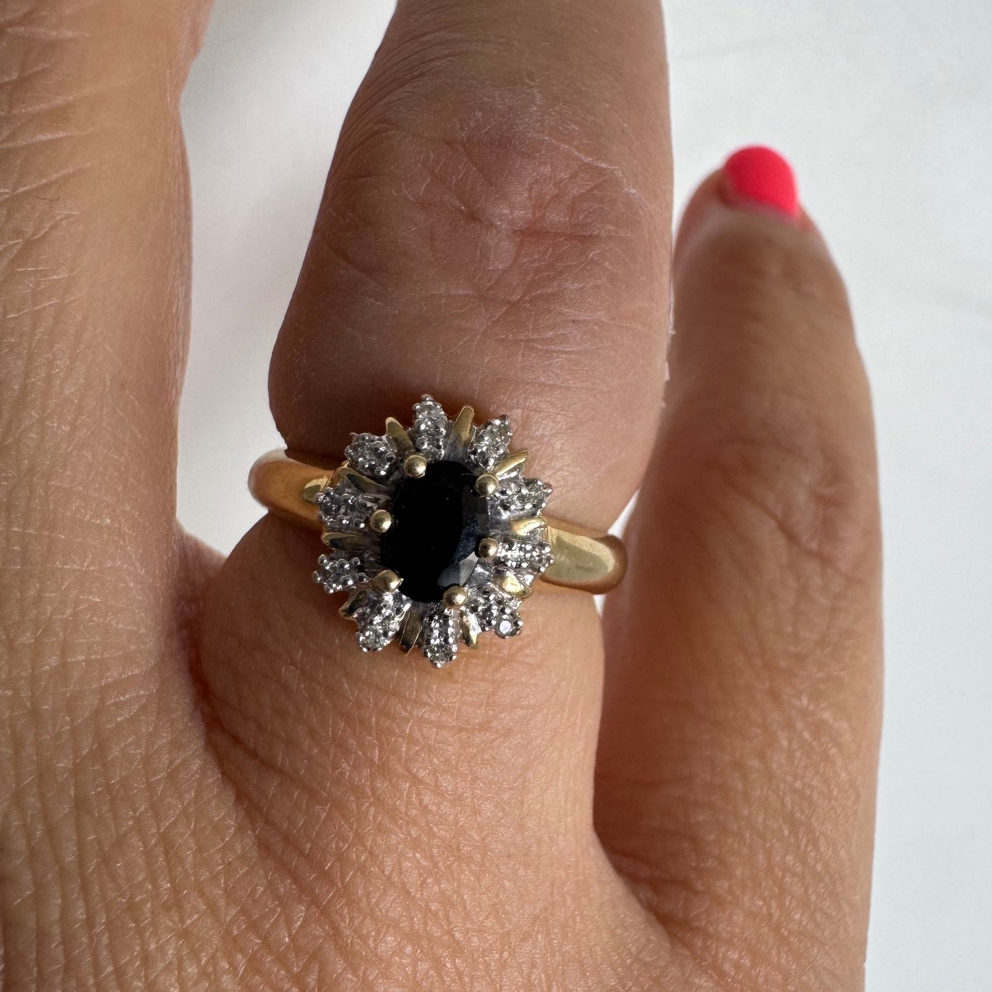 טבעת זהב צהוב 14 קראט משובצת אבן ספיר מרכזית בחיתוך אובלי, המוקפת בהילה של יהלומים טבעיים נוצצים.