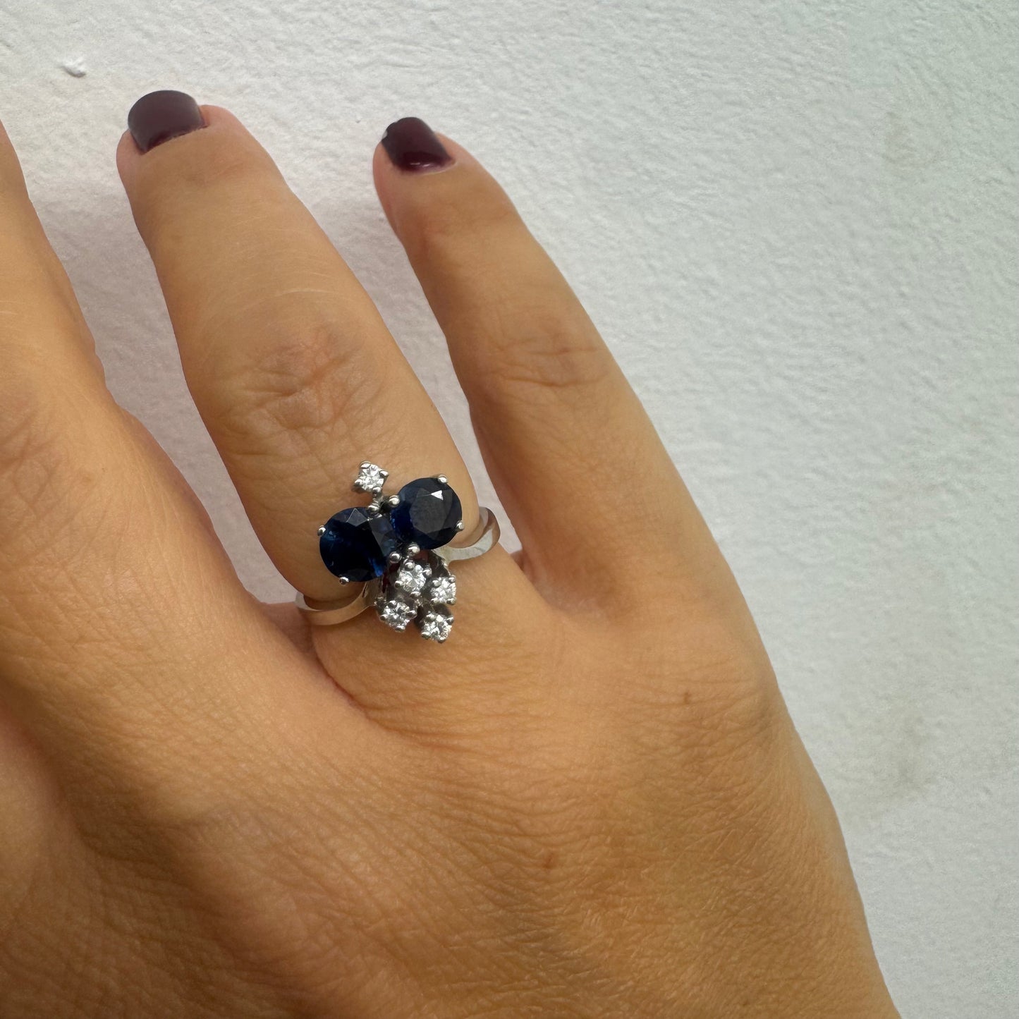 טבעת זהב לבן 14 קראט משובצת שתי אבני ספיר בגוון כחול עמוק ובאשכולות יהלומים לבנים מנצנצים.