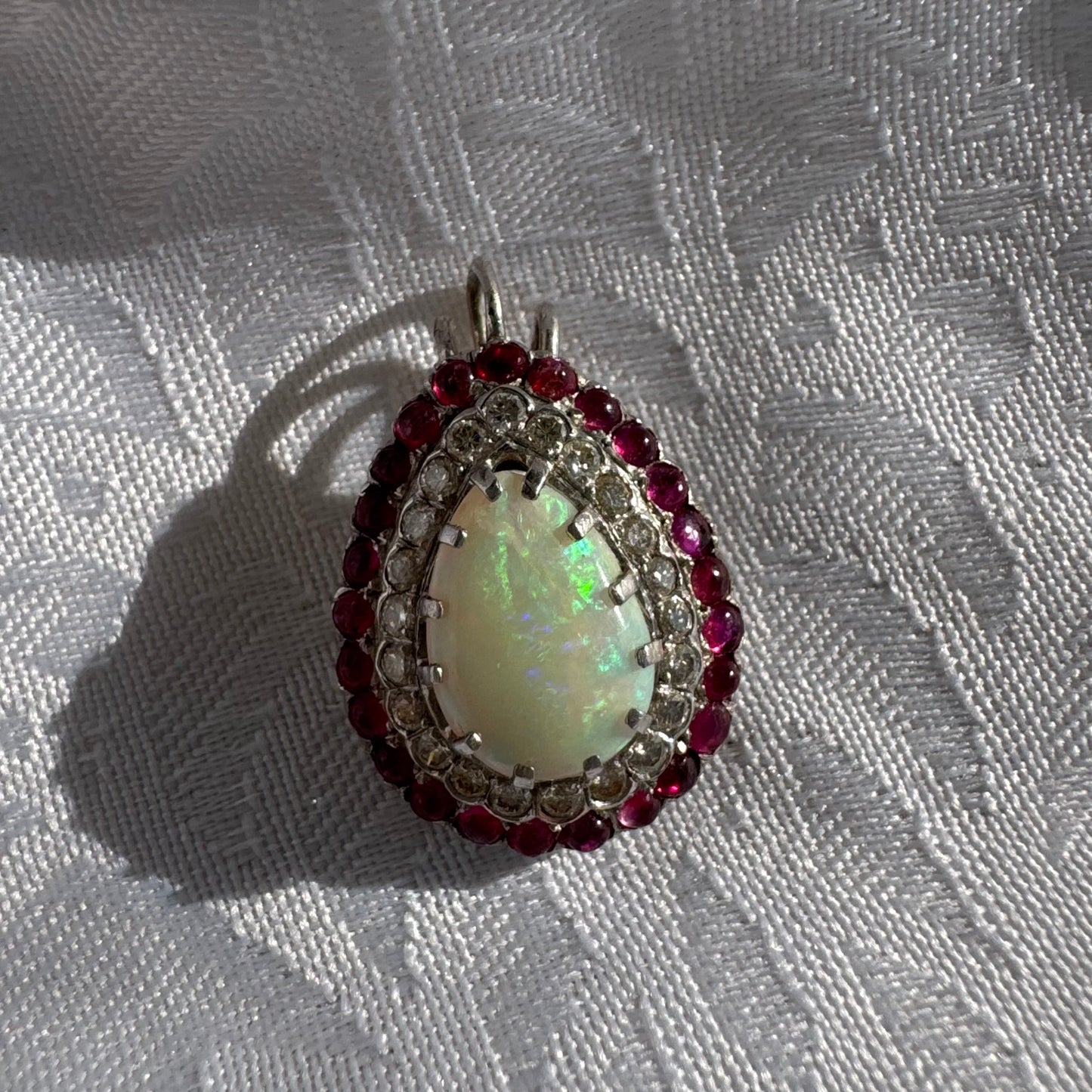 תליון זהב 14 קראט משובץ אבן אופל בחיתוך טיפה, מוקפת בשתי מסגרות של יהלומים ורובי נוצצים. 