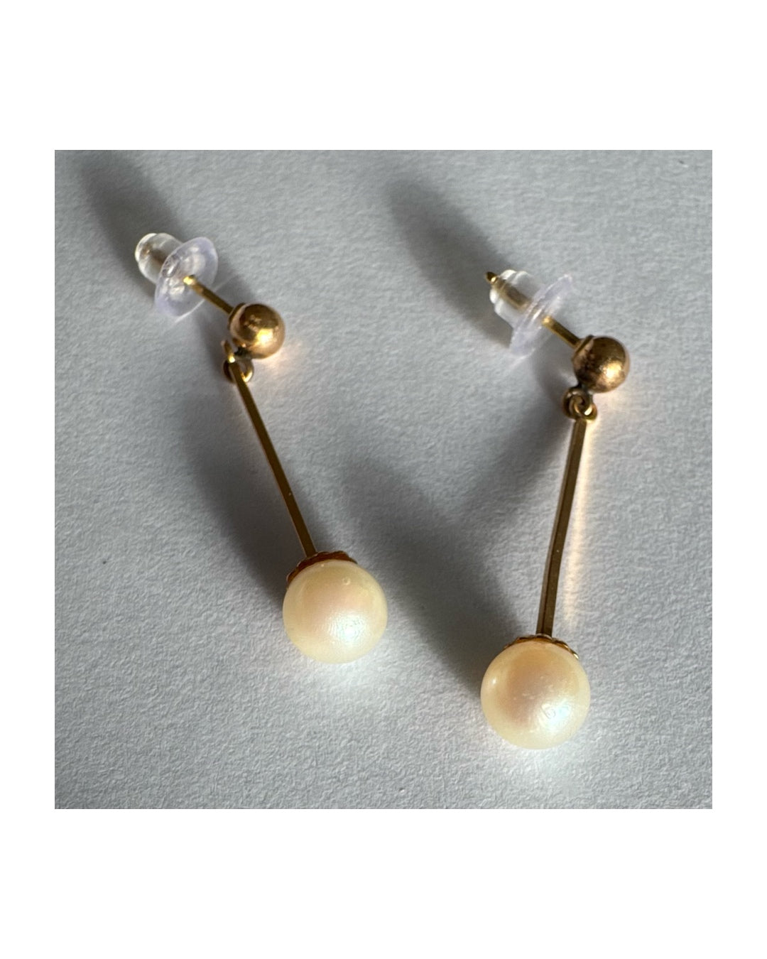 עגילי זהב 14 קראט בעיצוב תלוי ועדין, עם פנינה עגולה בקצה.