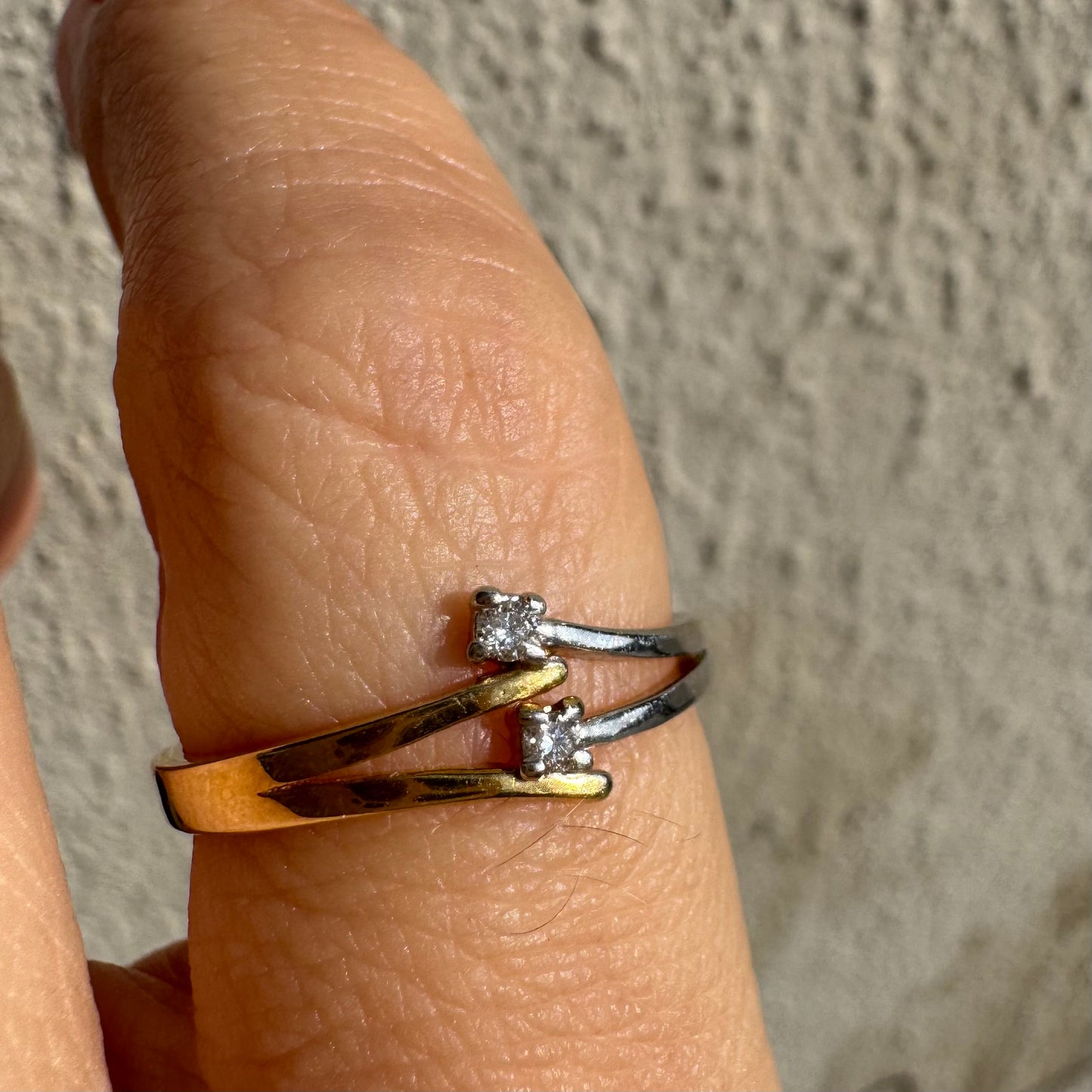 טבעת זהב 14 קראט, עם זרועות מצטלבות בזהב צהוב וזהב לבן, שכל אחת מהן משובצת יהלום קטן ונוצץ.