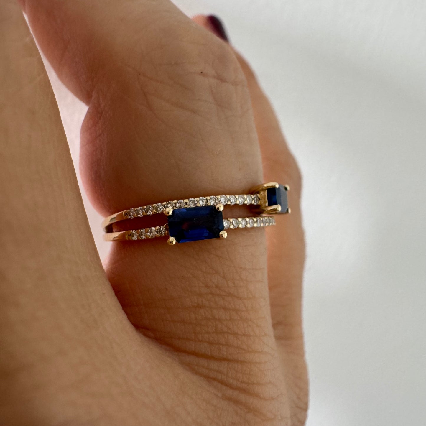 טבעת זהב צהוב 14 קראט בעיצוב פתוח, משובצת שתי אבני ספיר בחיתוך אמרלד ושורות יהלומים עדינים.