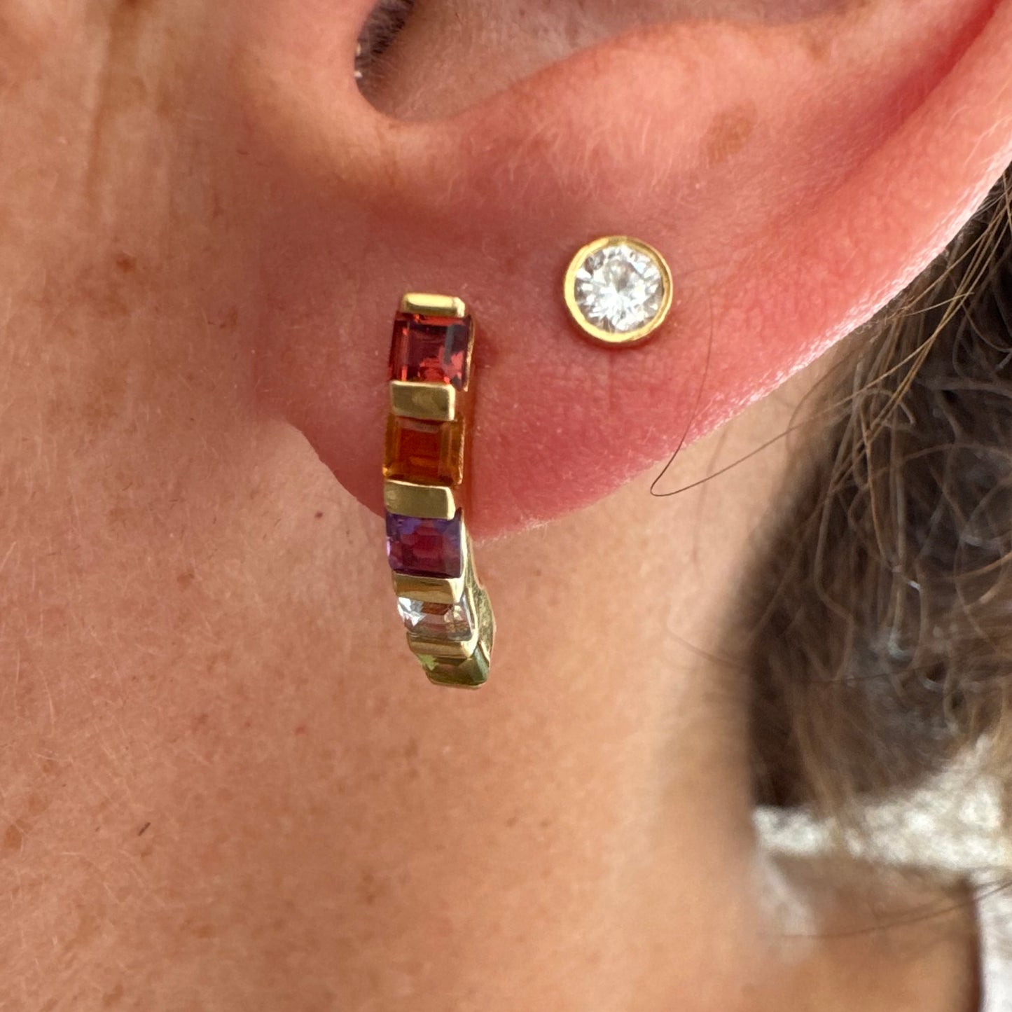 18K gold hoop earrings set with a vibrant line of multi-colored gemstones — including Garnet, Citrine, Amethyst, Peridot, and Blue Topaz.