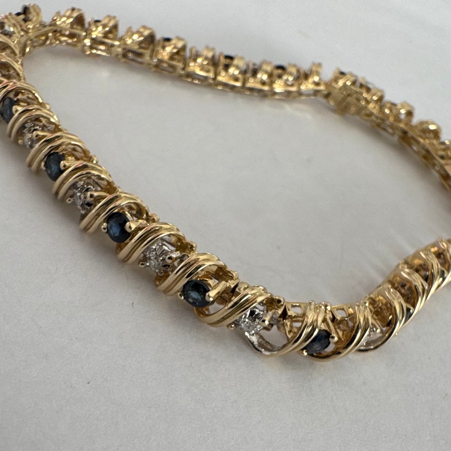 צמיד זהב צהוב 14 קראט משובץ אבני ספיר כחולות ויהלומים, המשובצים בעיצוב זורם עם קווים מעוגלים העוטפים כל אבן.