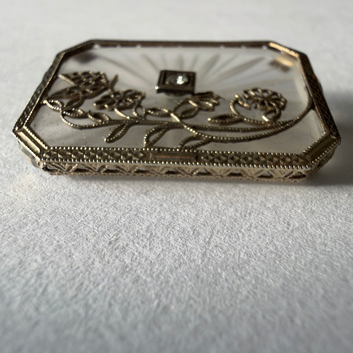 An antique Art-Deco brooch featuring a geometric design, delicate floral details & a sparkling Diamond