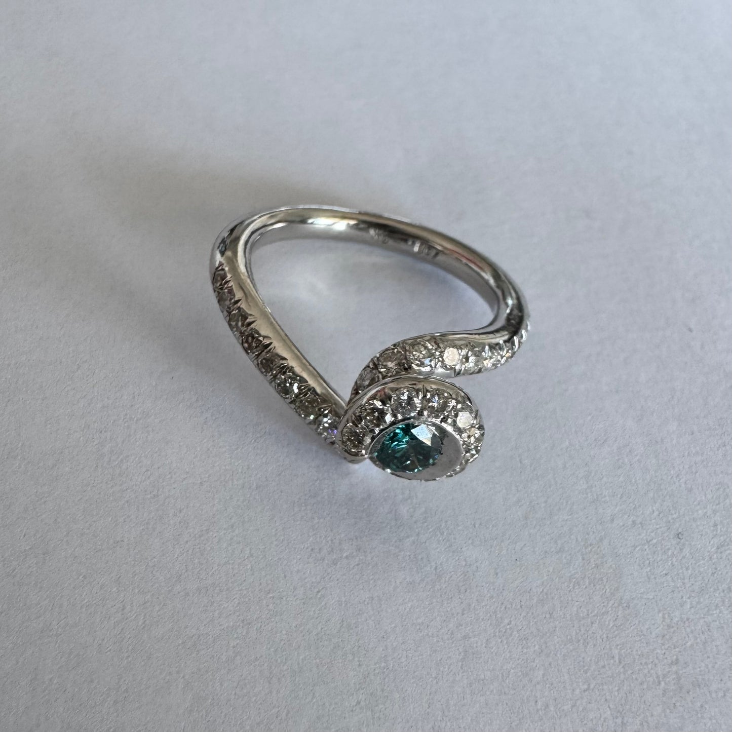 טבעת זהב לבן 18 במרכזה משובץ יהלום כחול עז, מוקף בהילה של יהלומים לבנים והזרועות של הטבעת משובצות יהלומים