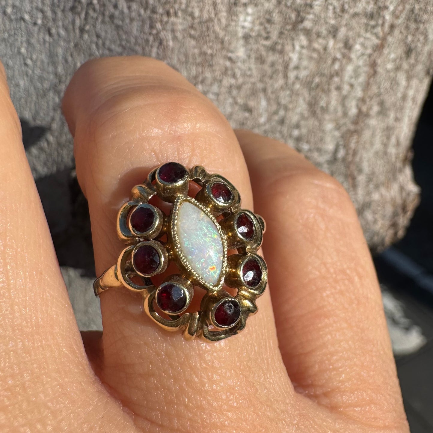 14K gold ring set with a luminous marquise-cut Opal at the center, surrounded by deep red Garnet cabochons