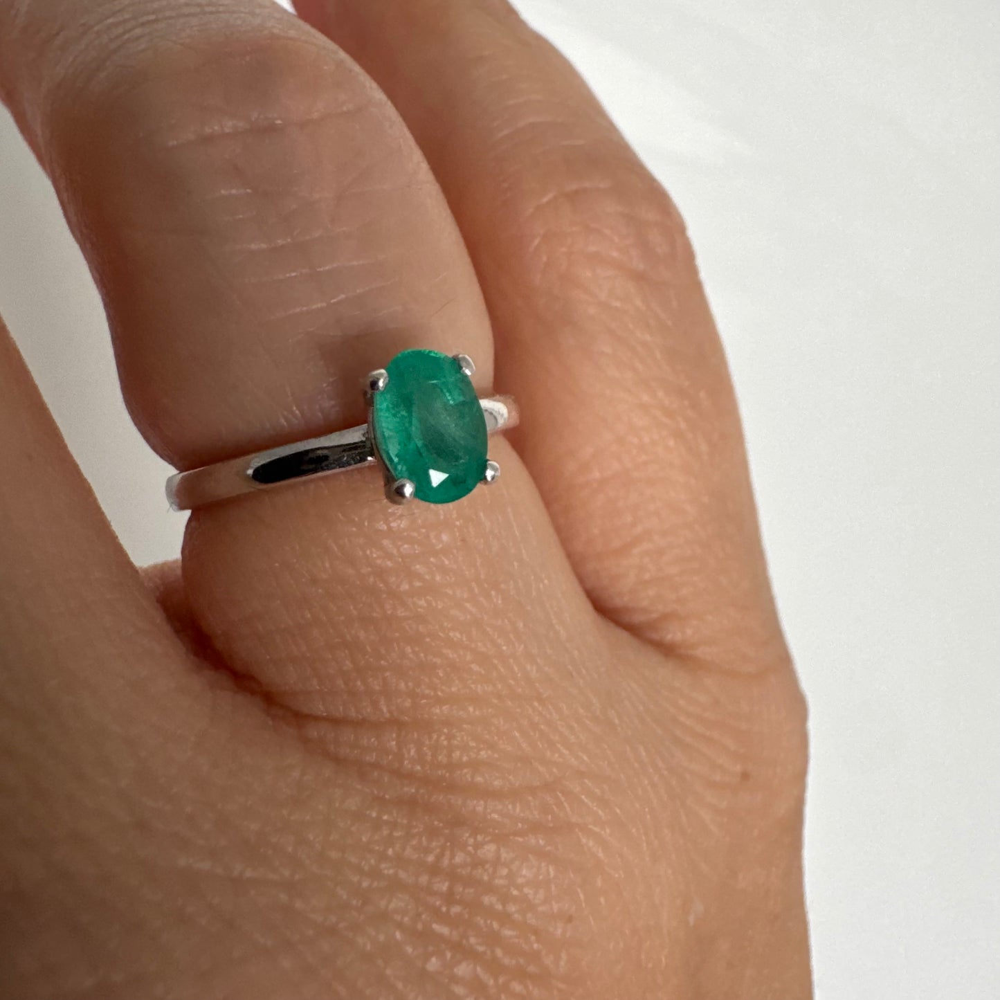 טבעת זהב לבן 14 קראט משובצת אבן אמרלד אובלית בגוון ירוק עשיר.