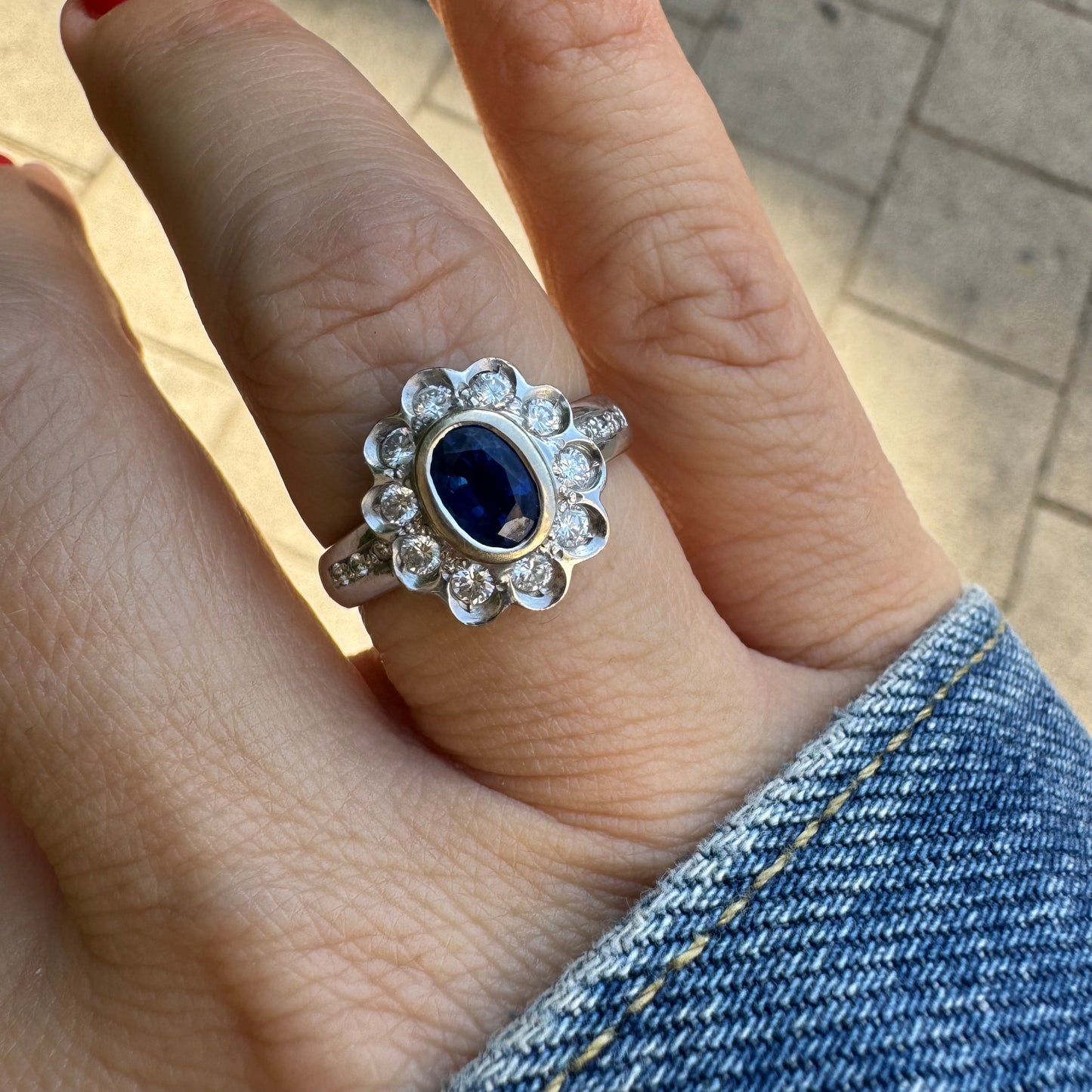 18K gold ring set with an oval blue Sapphire surrounded by a halo of round Diamonds in a flower-shaped design.