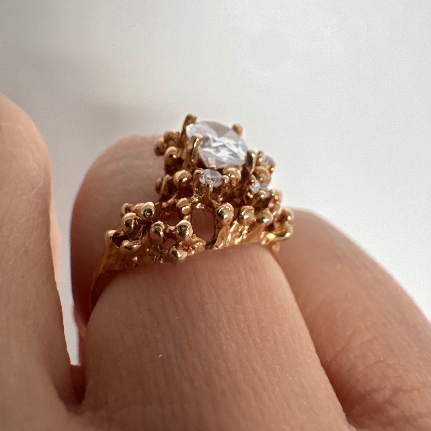 14K gold ring set with a central oval clear stone, accented by additional clear stones in an open, organic design.