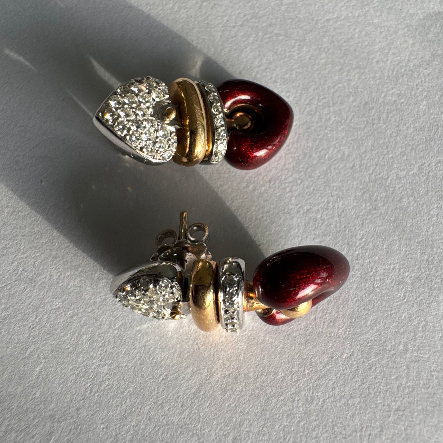 עגילי זהב 18 קראט בשילוב זהב צהוב ולבן, משובצים יהלומים בחלק העליון ובחישוק מרכזי, ובתחתית תליון לב אדום בגימור מבריק.