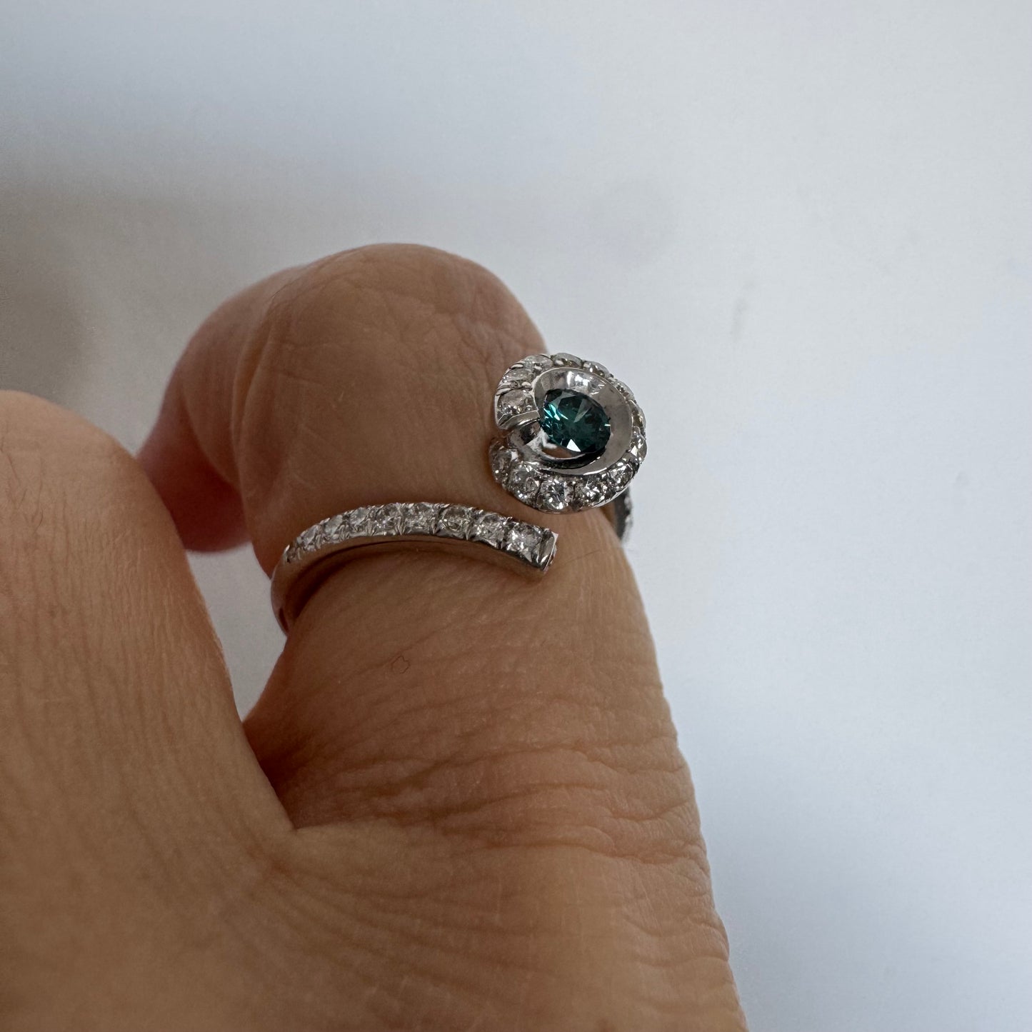 טבעת זהב לבן 18 במרכזה משובץ יהלום כחול עז, מוקף בהילה של יהלומים לבנים והזרועות של הטבעת משובצות יהלומים