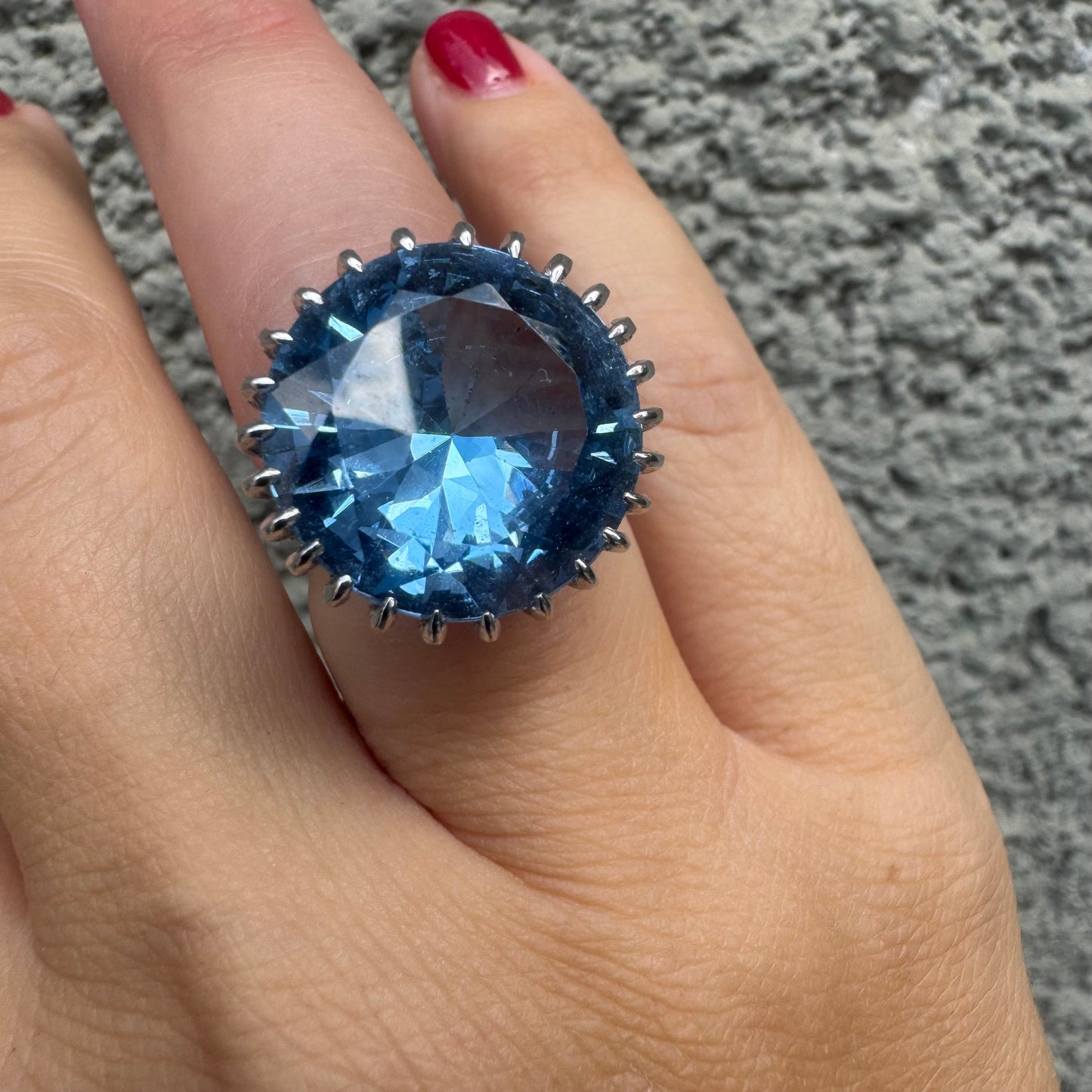 טבעת זהב לבן 14 קראט משובצת אבן טופז בצבע כחול, בולטת, בחיתוך עגול, משובצת במסגרת שיניים גבוהה ליצירת מראה מרשים ותופס עין
