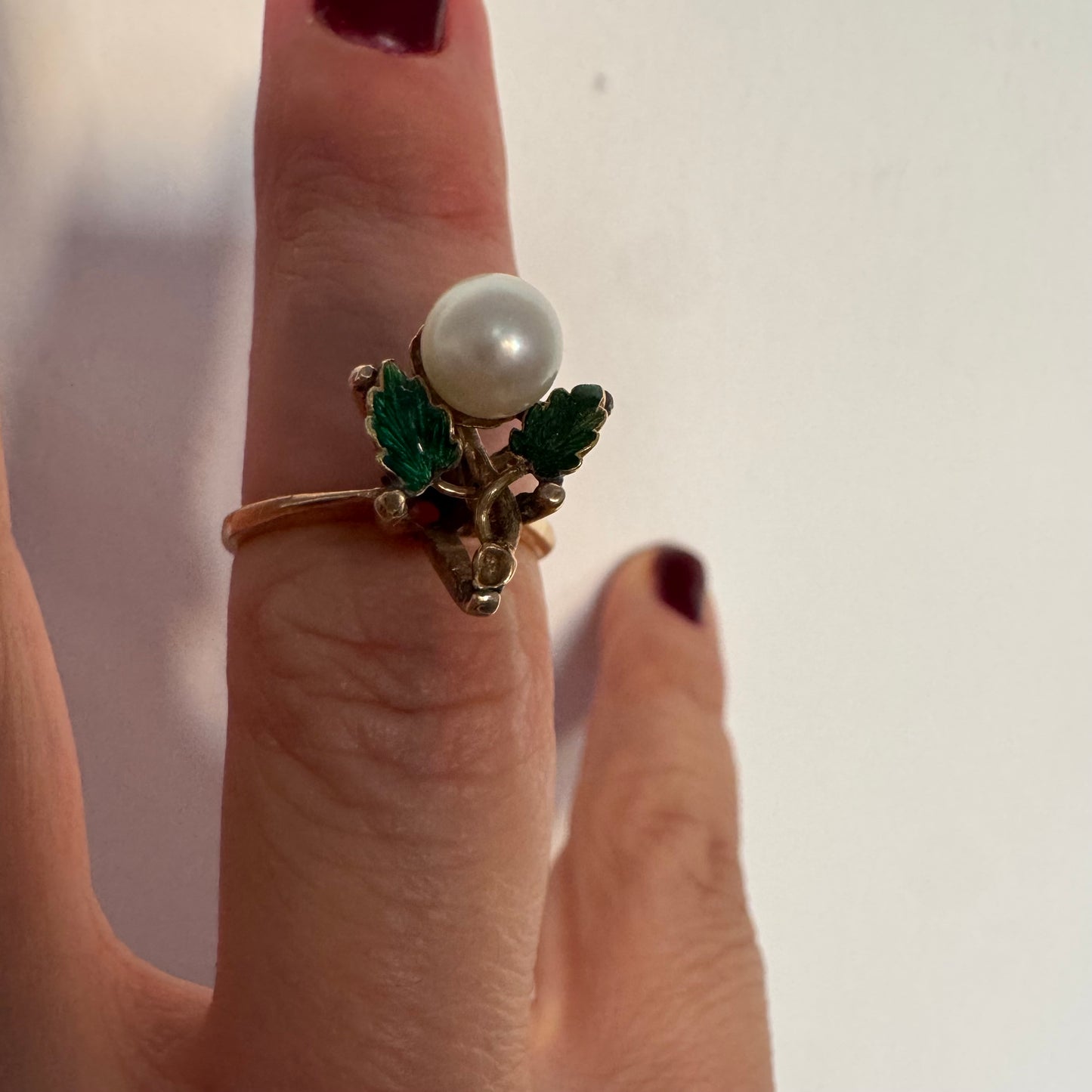 טבעת זהב 14 קראט משובצת פנינה מרכזית ומעוטרת אמייל ירוק בעבודת יד בצורת עלים.