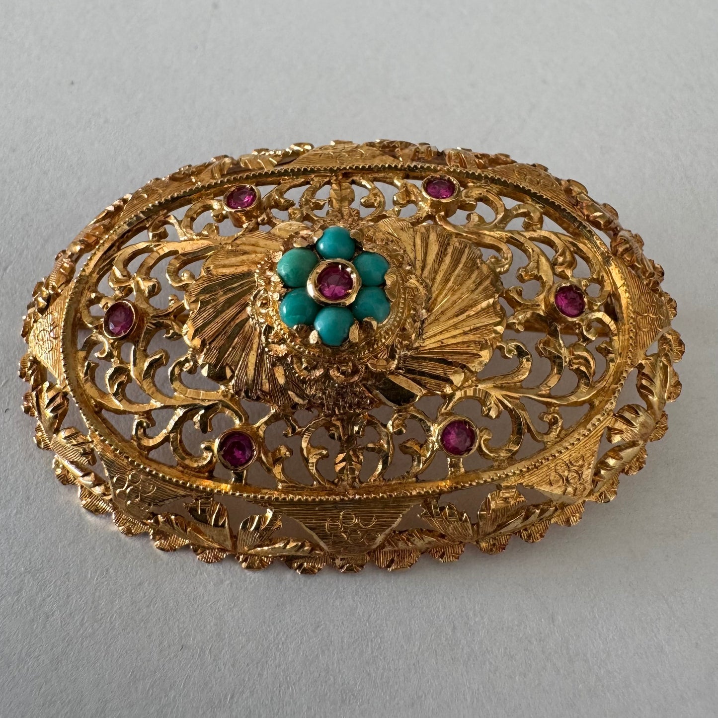 18K gold filigree brooch featuring intricate openwork detailing, accented with Ruby & Turquoise arranged in a floral centerpiece
