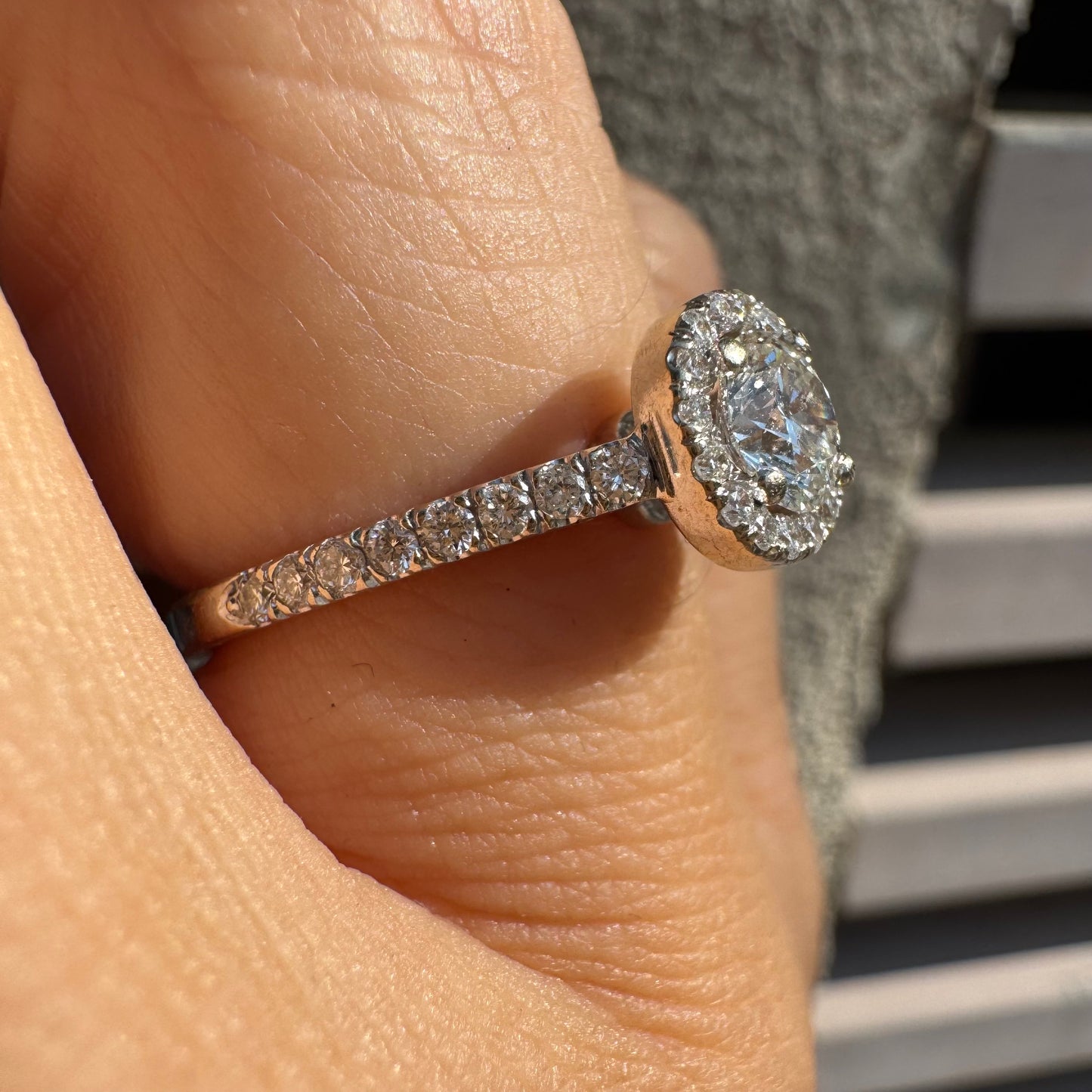 טבעת זהב לבן 14 קראט משובצת יהלום מרכזי עגול והילה נוצצת של יהלומים קטנים, עם יהלומים נוספים על החישוק.